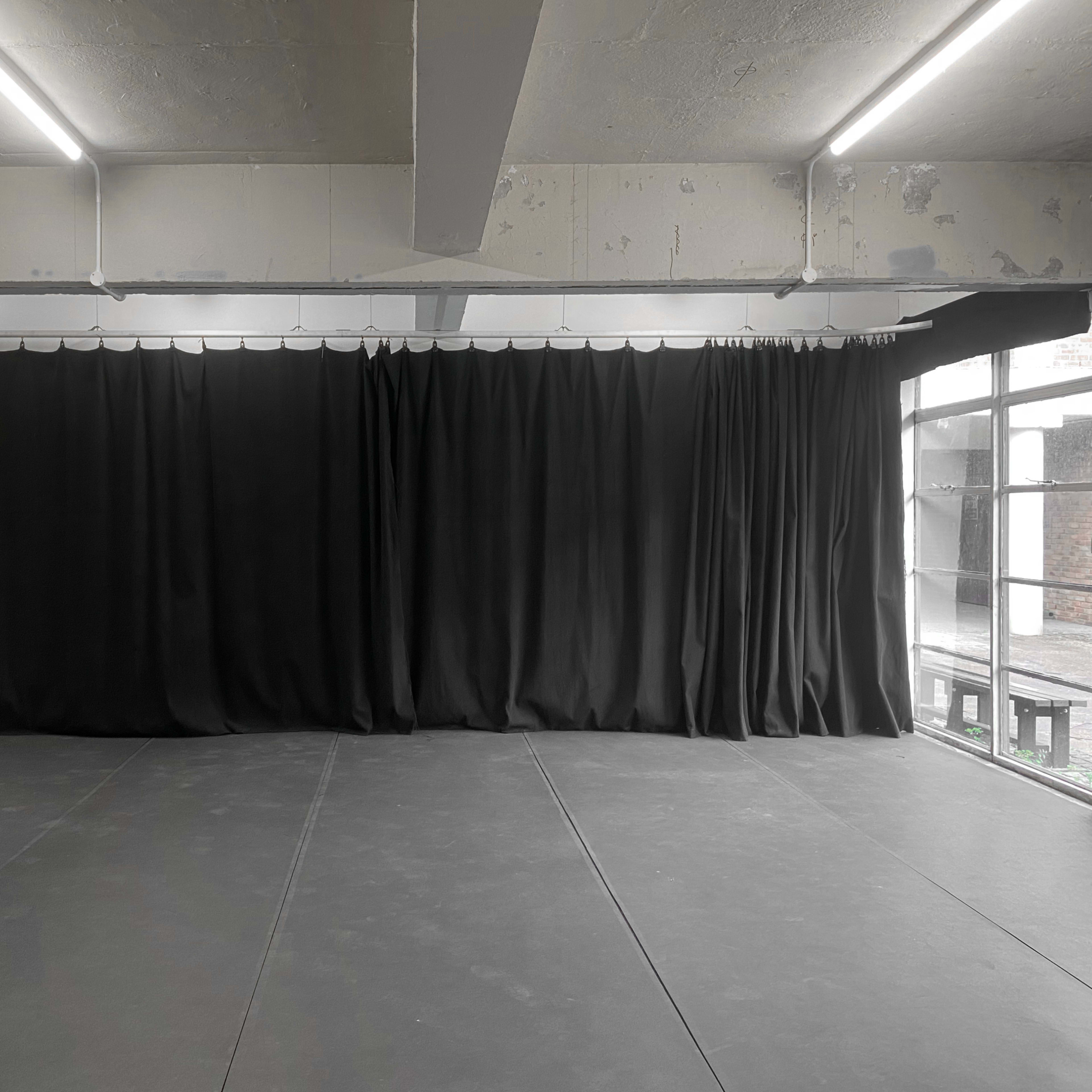 A spacious room with a dark floor and black curtains along one wall, illuminated by overhead lights.