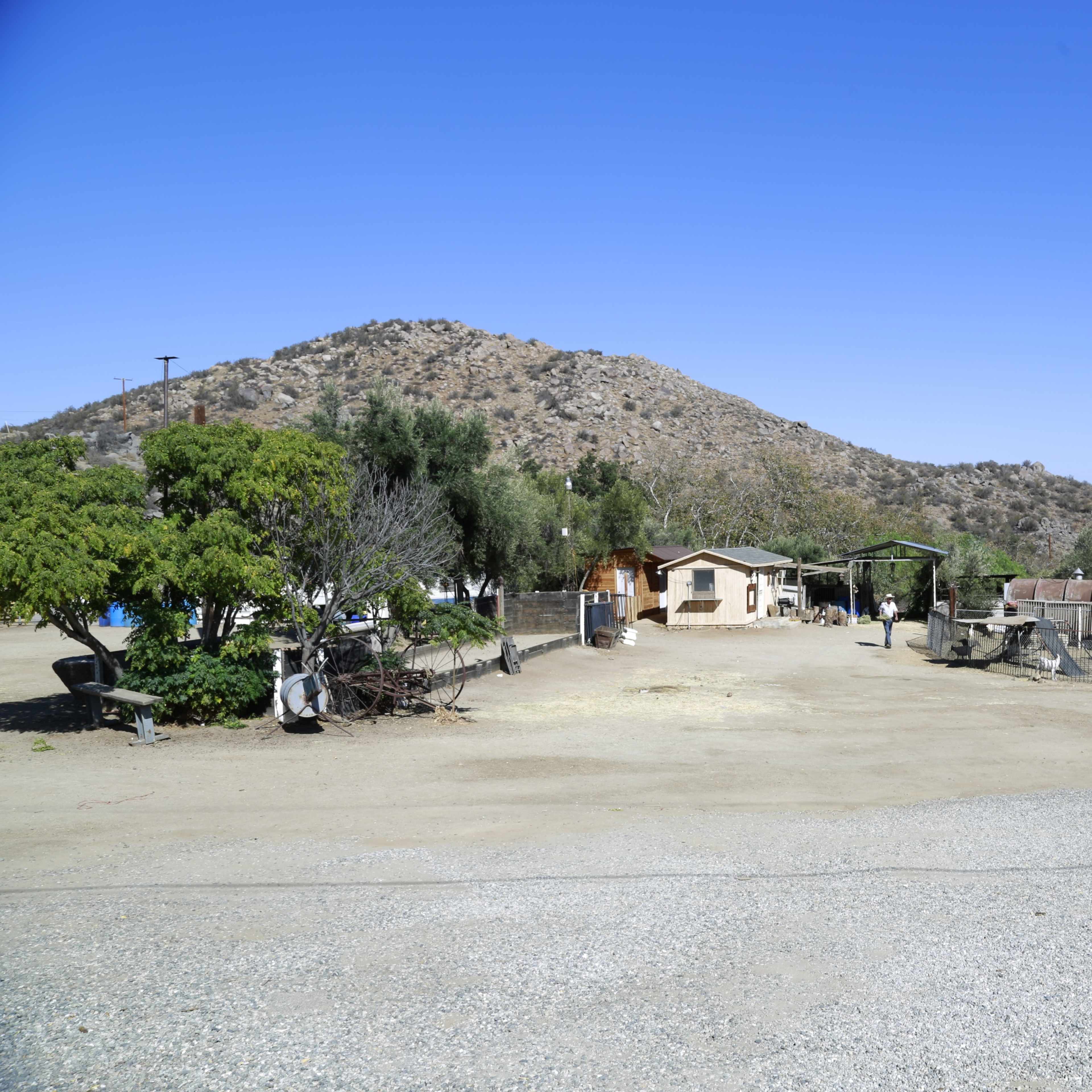 A rural landscape with a small house, various outbuildings, and a large mountain in the background.