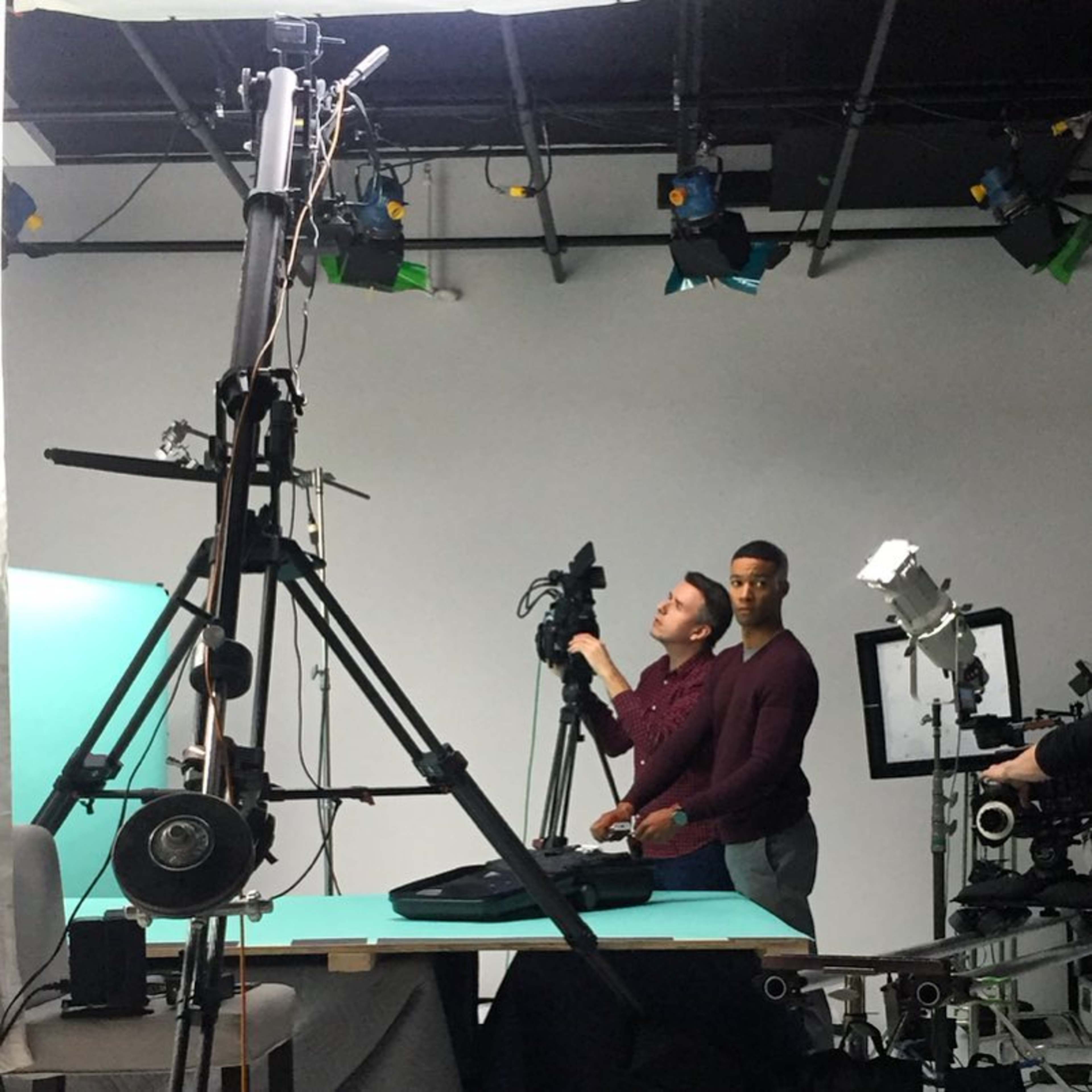 Two men operate camera equipment in a studio setting with various lighting and support rigs.