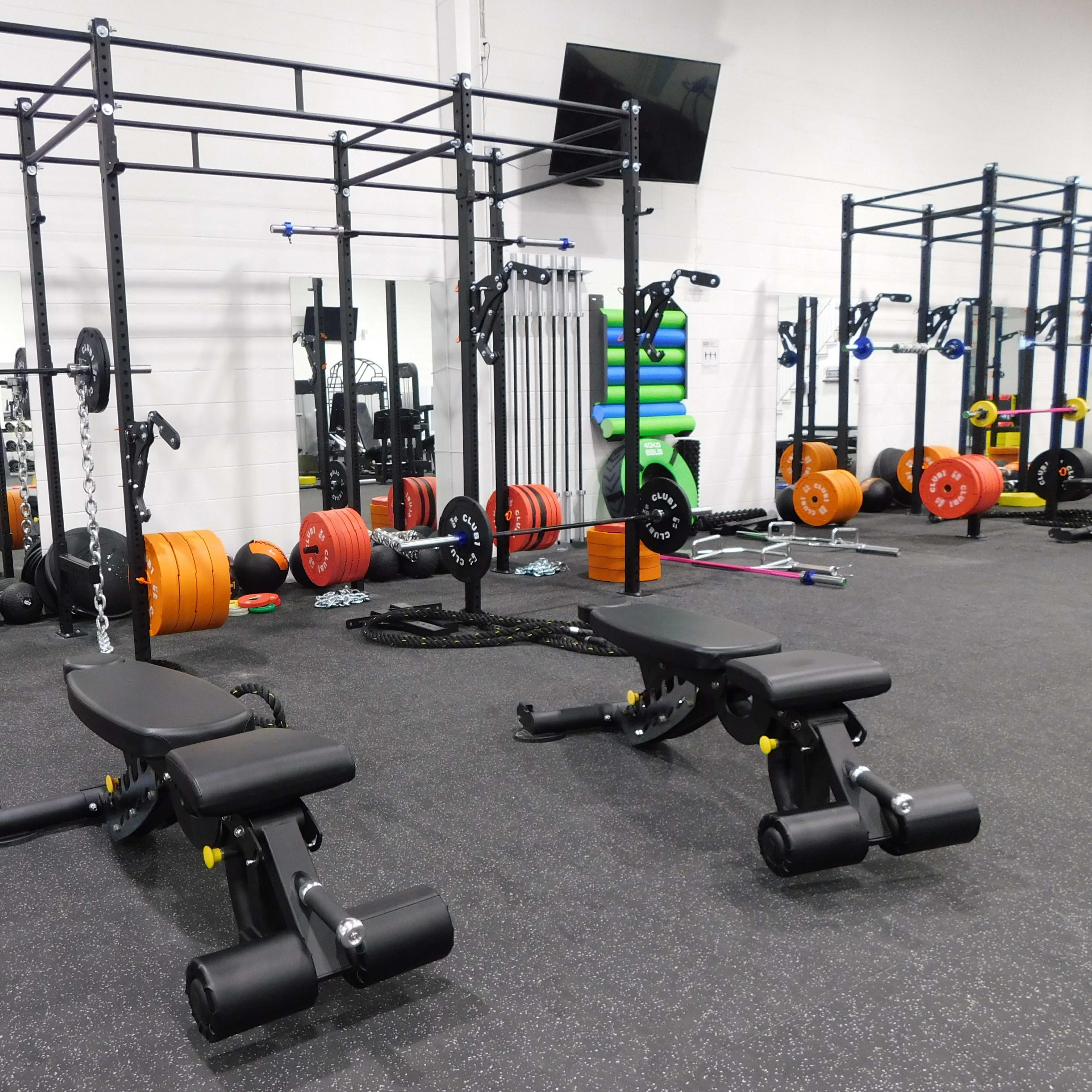 A modern gym with weight benches, various weights, and strength training equipment arranged across the room.