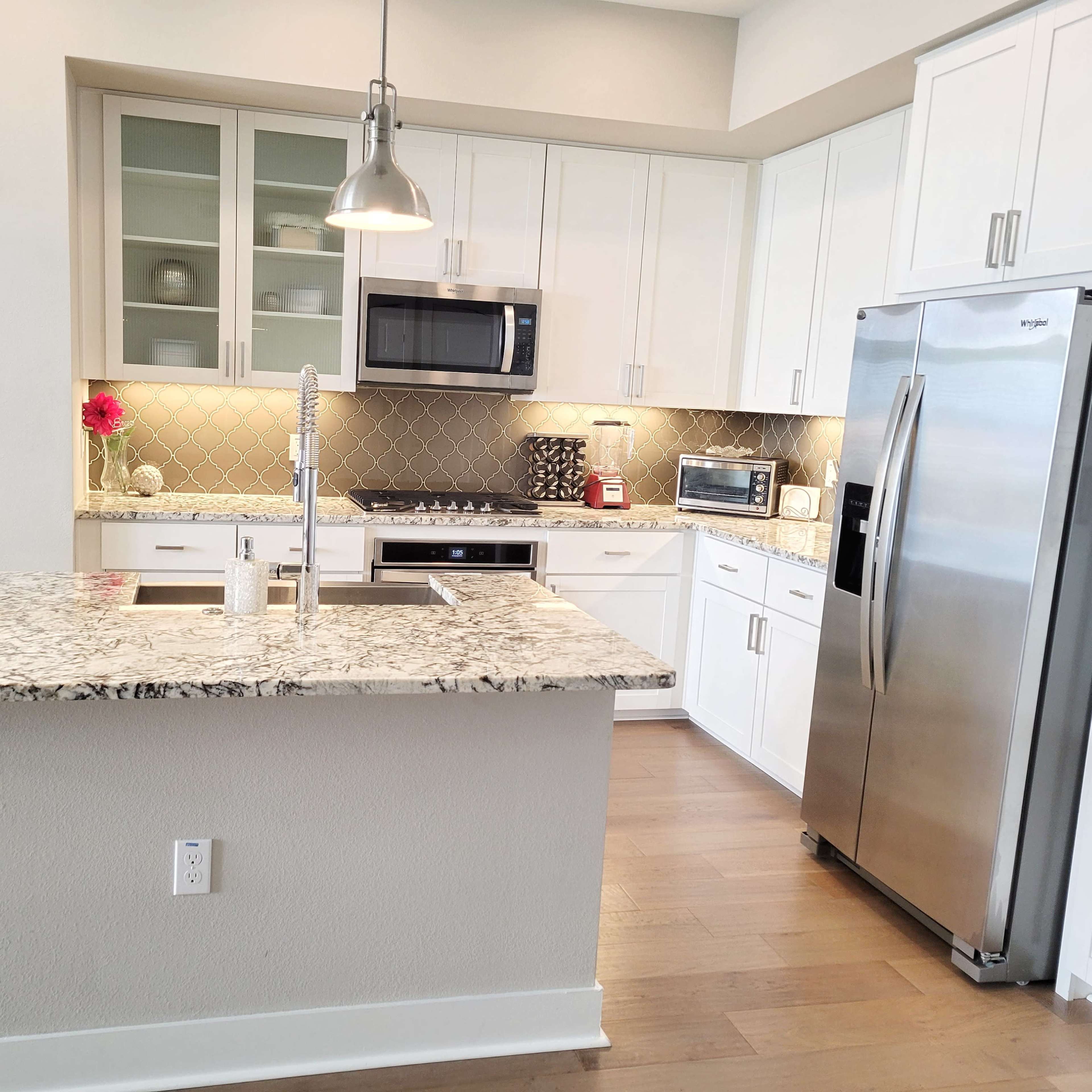 A modern kitchen with white cabinetry, a large granite island, stainless steel appliances, and a decorative plant on the countertop.