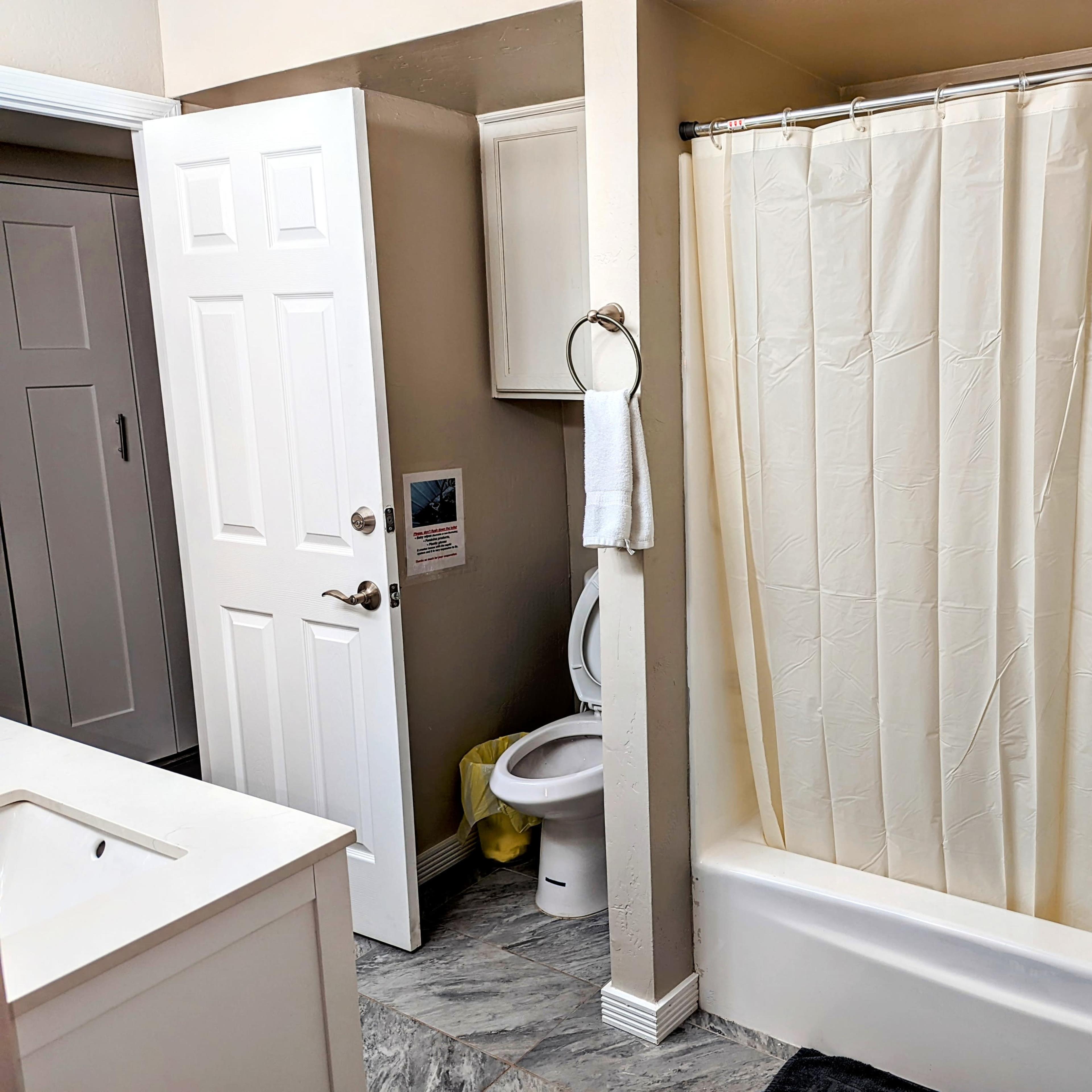 A bathroom with a shower curtain, a toilet, a sink, and a door leading to another room.