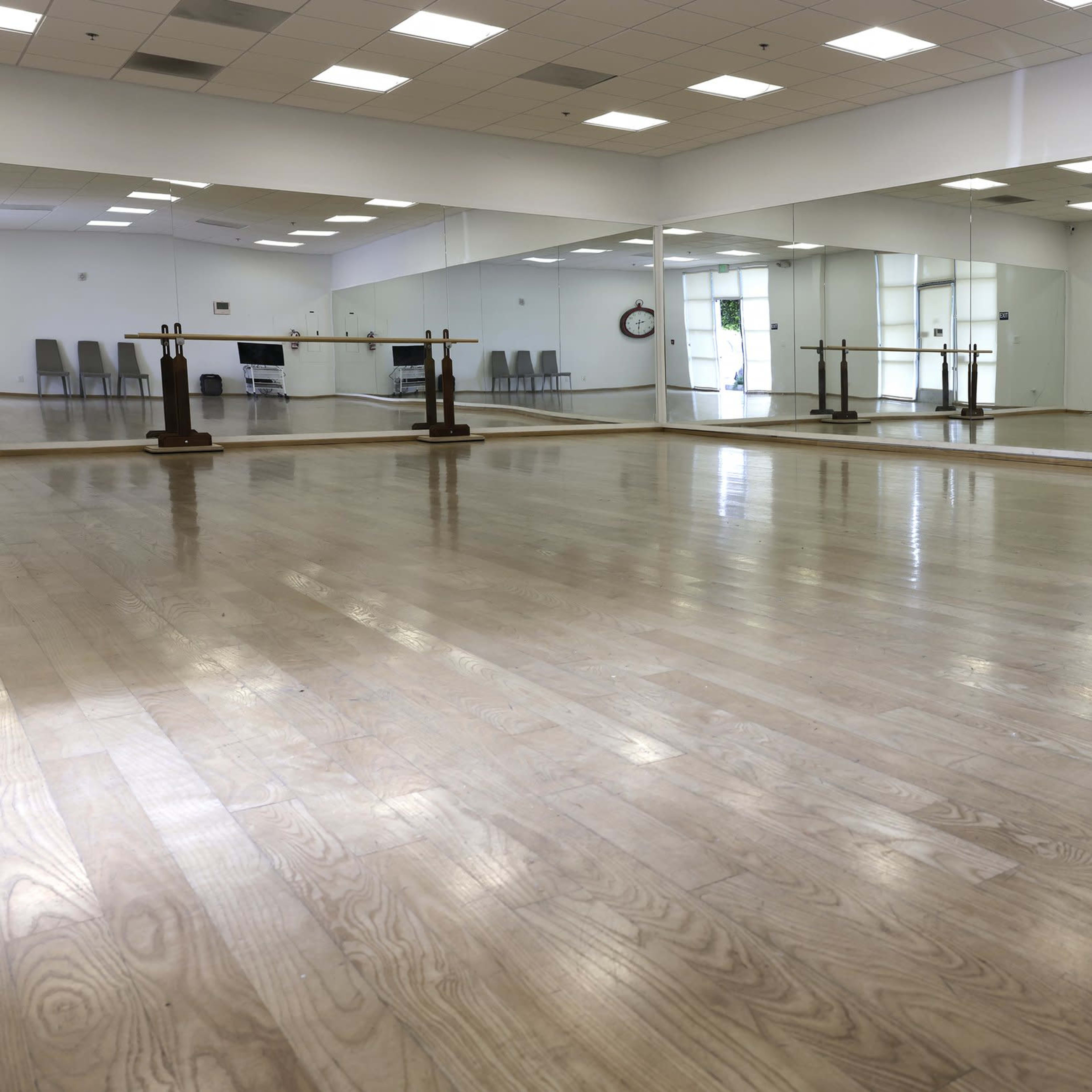 A spacious dance studio with polished wooden floors and large mirrors along one wall.