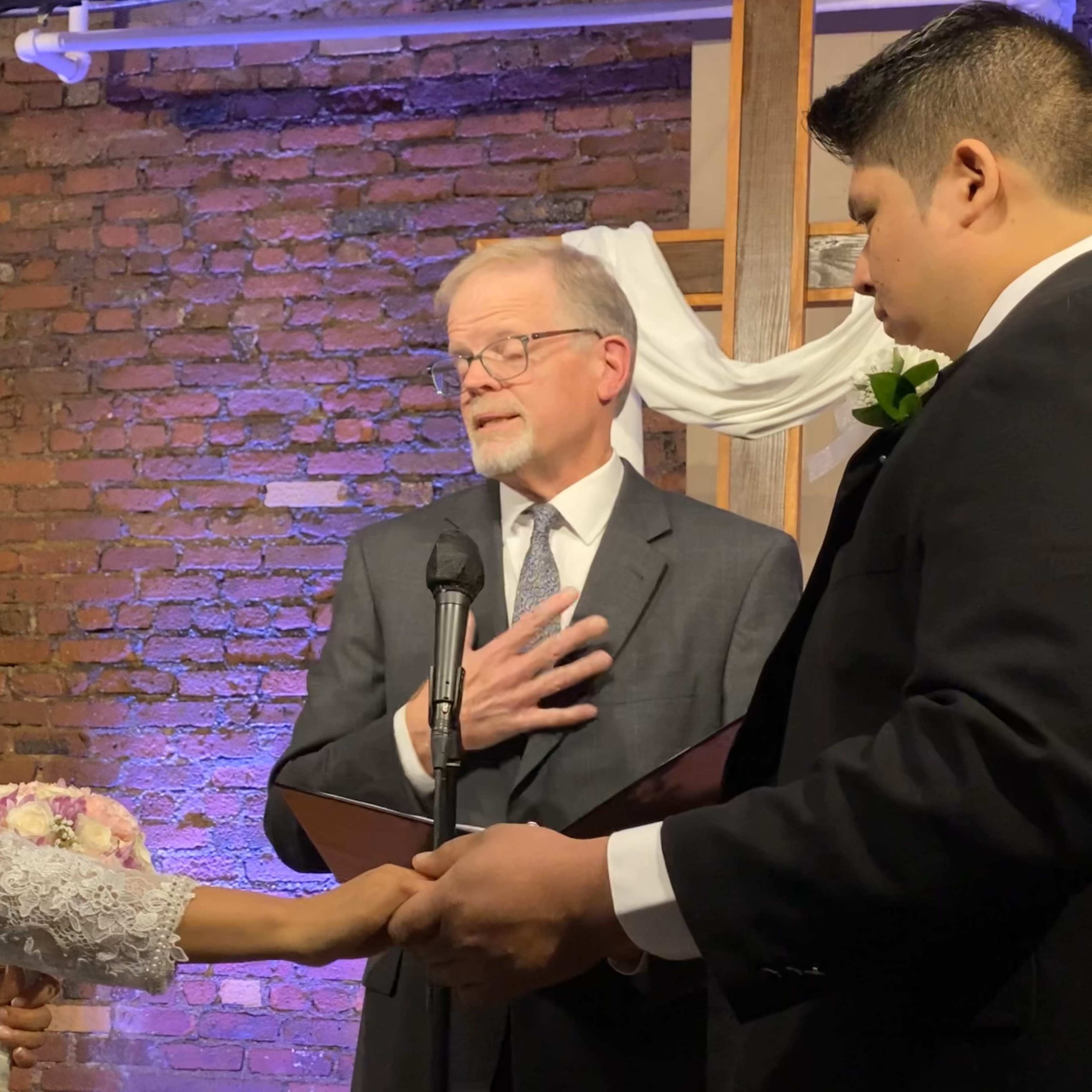 A bride and groom exchange vows during their wedding ceremony, while a officiant stands before them.