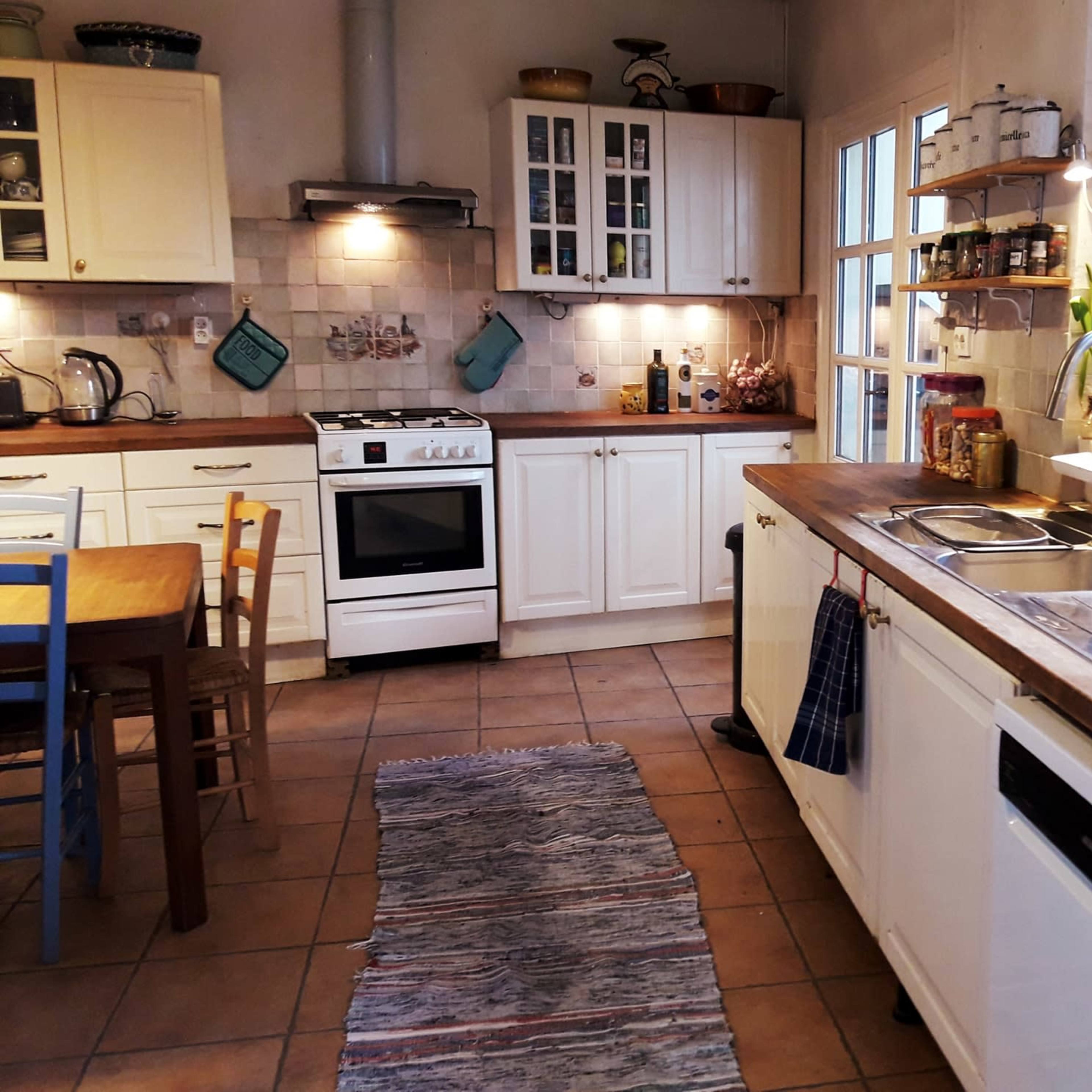 A bright kitchen features white cabinets, a wooden countertop, a stove, and a dining table with chairs.