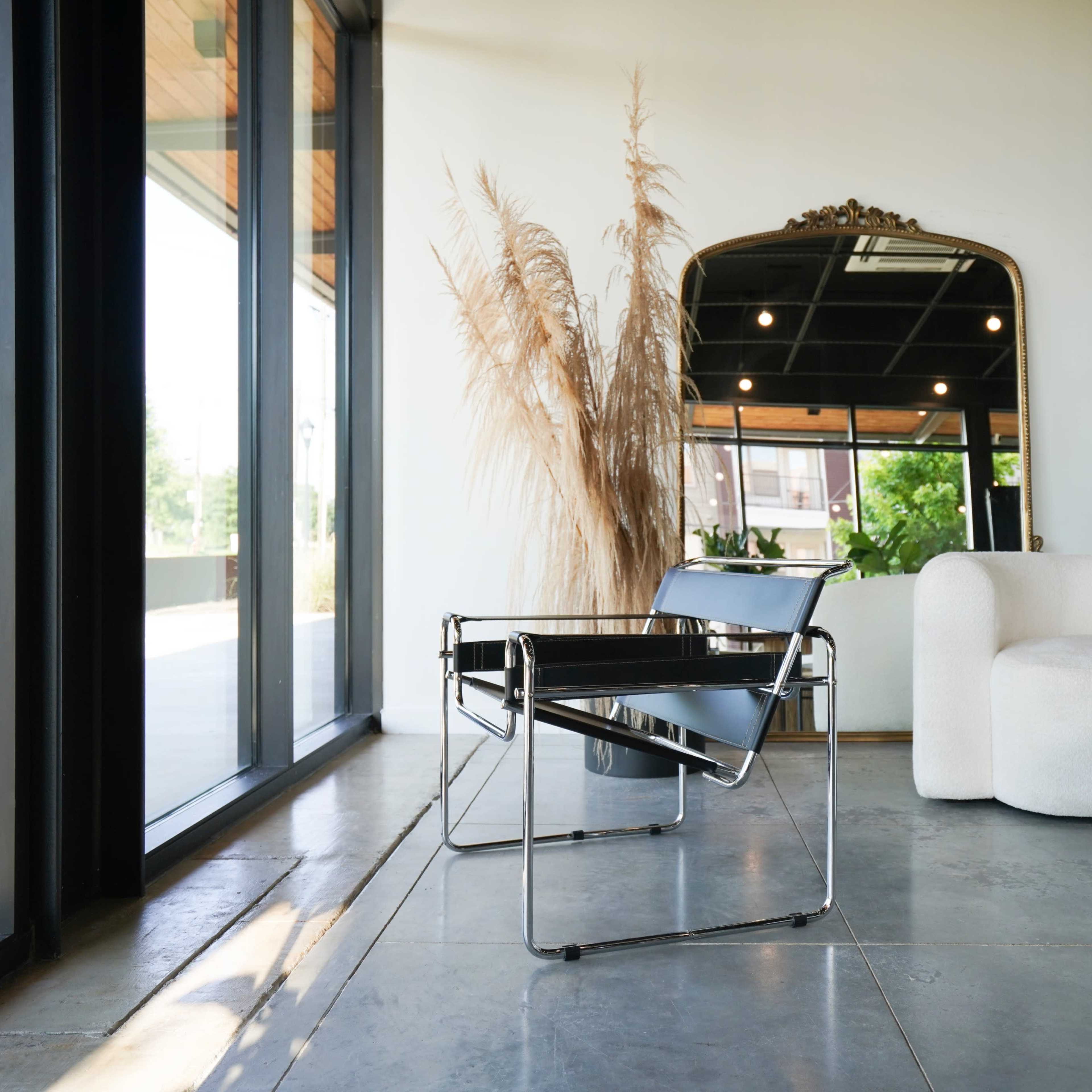 A modern living space featuring a minimalist chair, a round table with a magazine, and large windows allowing natural light to enter.