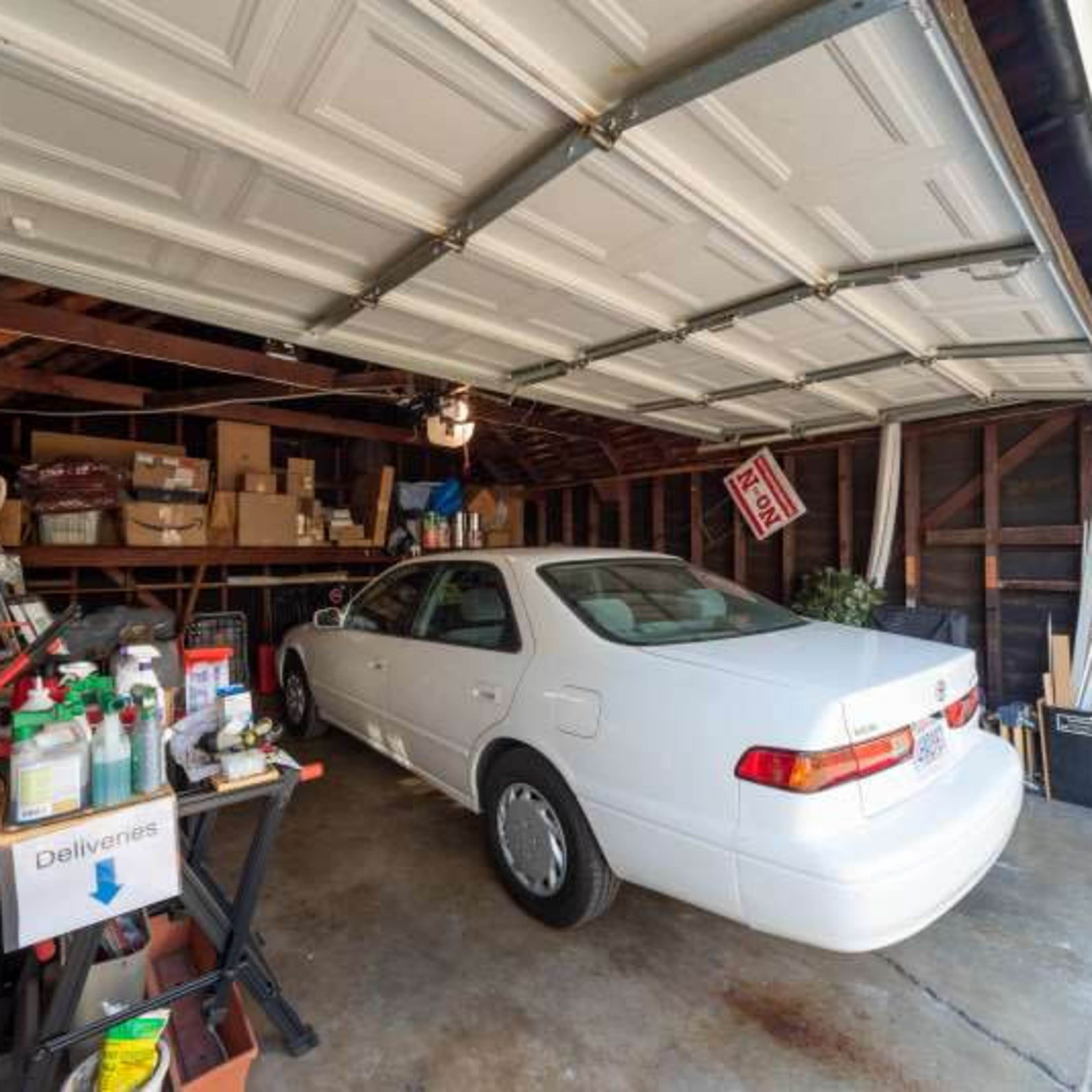 A white car is parked in a cluttered garage filled with boxes and various tools.