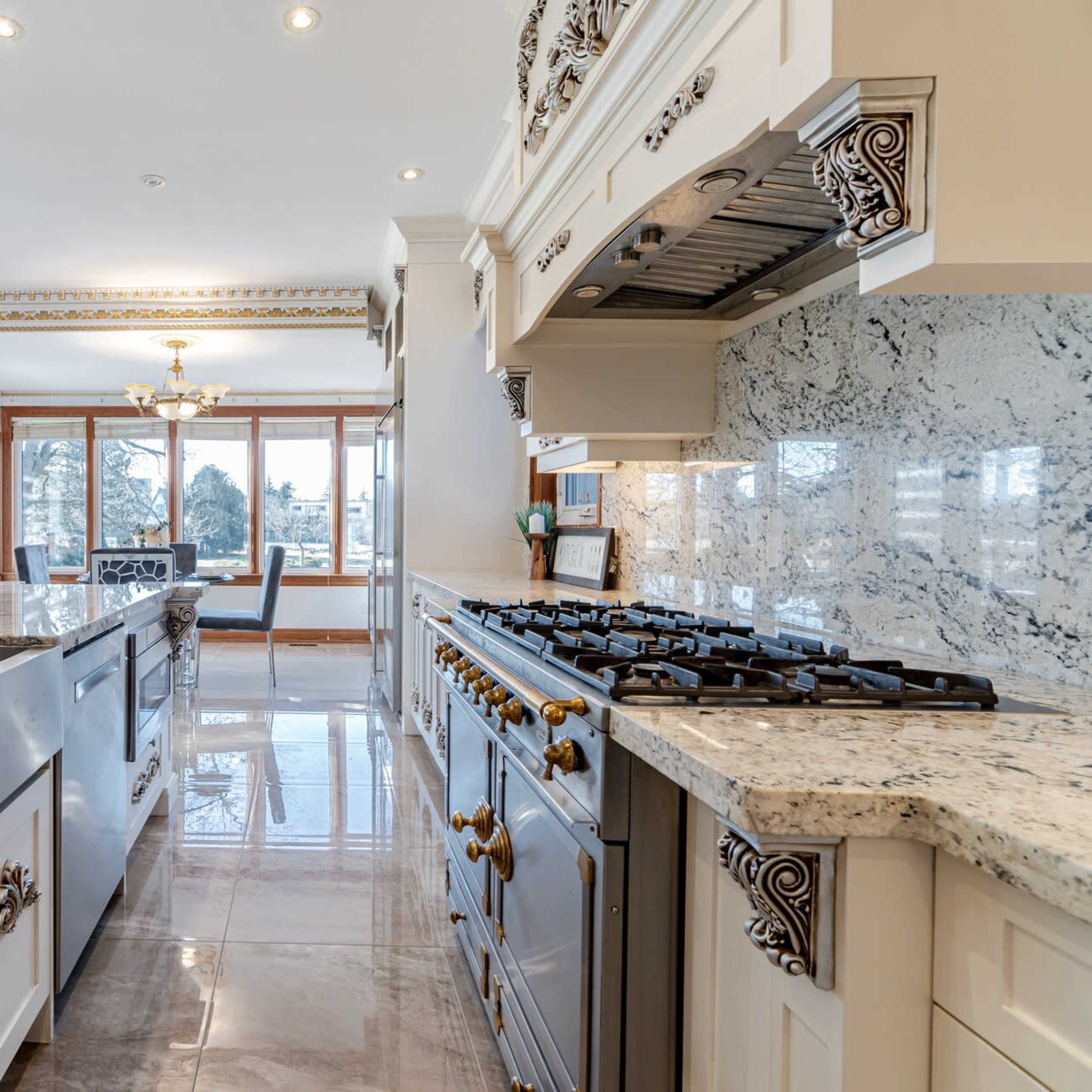 A spacious kitchen featuring a large farmhouse sink, a professional-grade gas stove, and marble countertops.