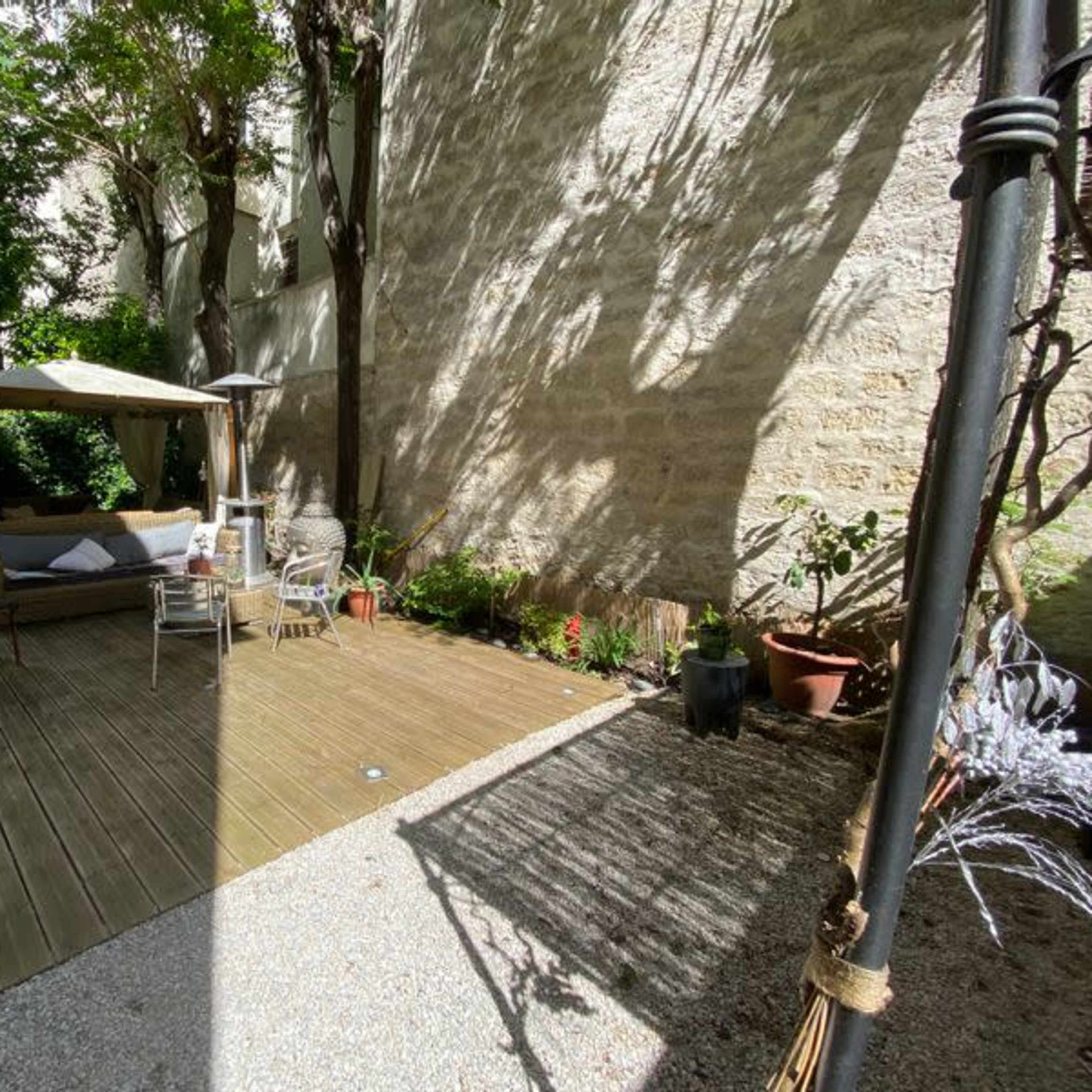 A wooden deck area with a canopy, outdoor seating, and various plants against a stone wall.