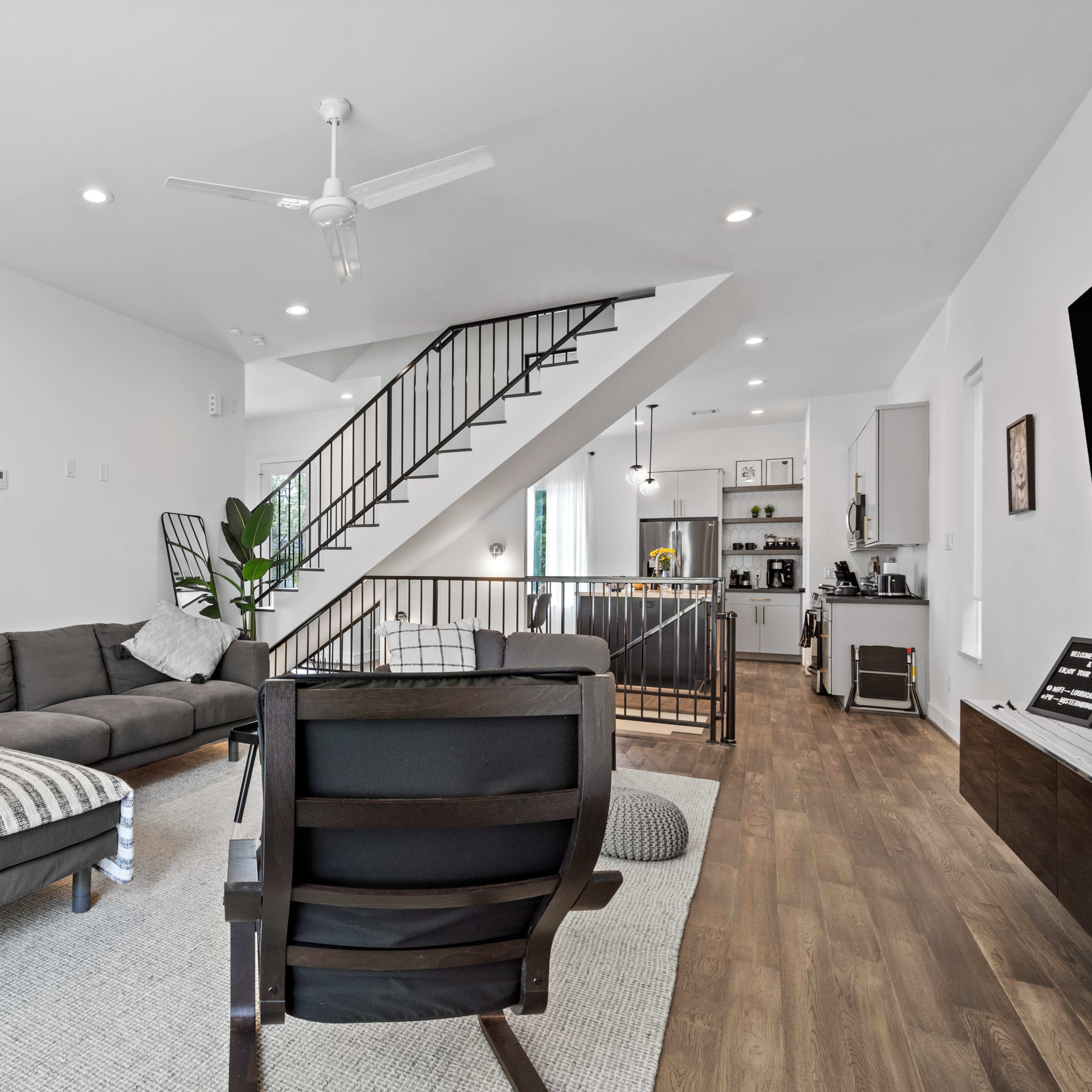 A modern living room with a sectional sofa, a chair, and a staircase leading to an upper level, all set against a backdrop of light-colored walls and hardwood flooring.