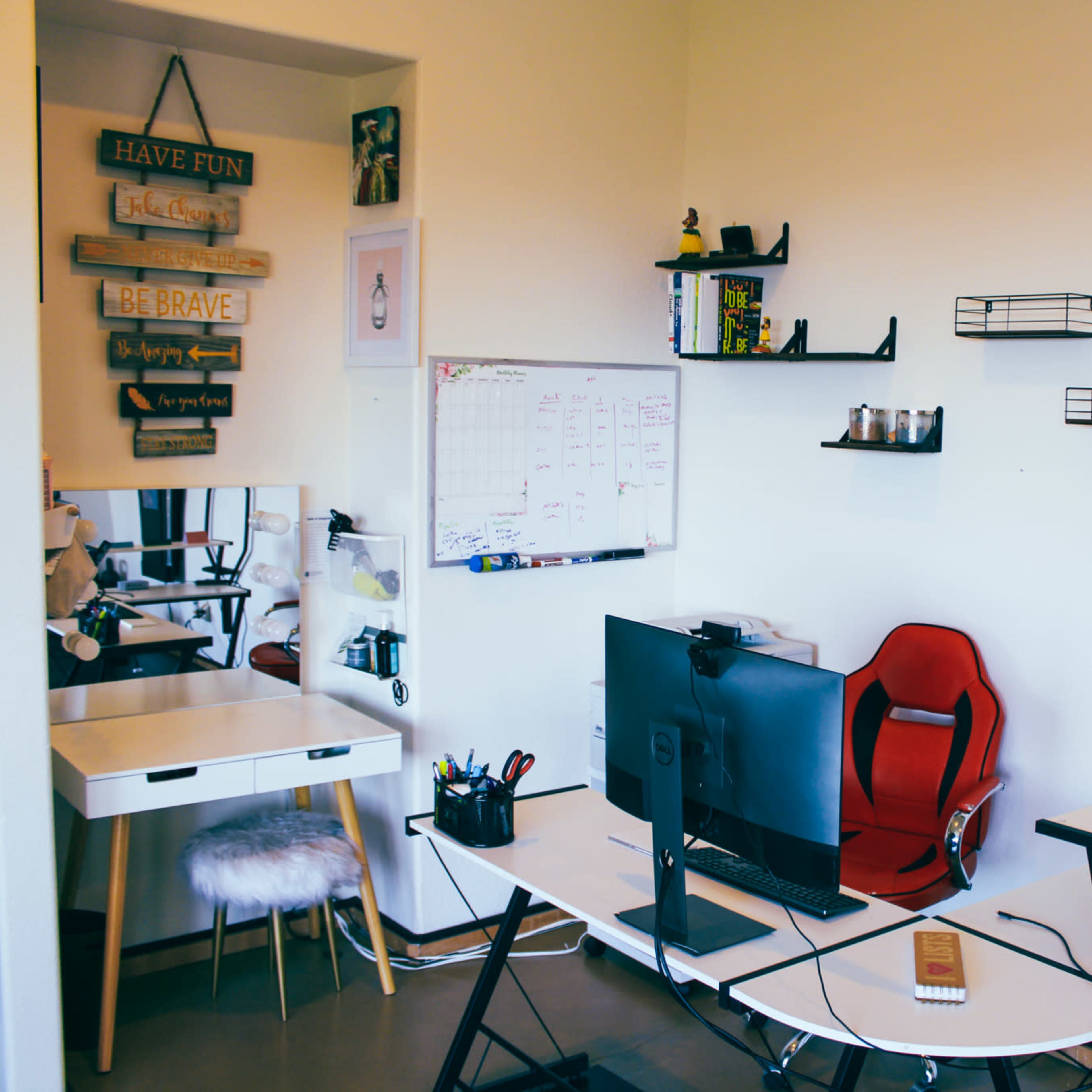 A modern workspace featuring a desk with a computer, a red ergonomic chair, wall shelves, and a whiteboard with a calendar.