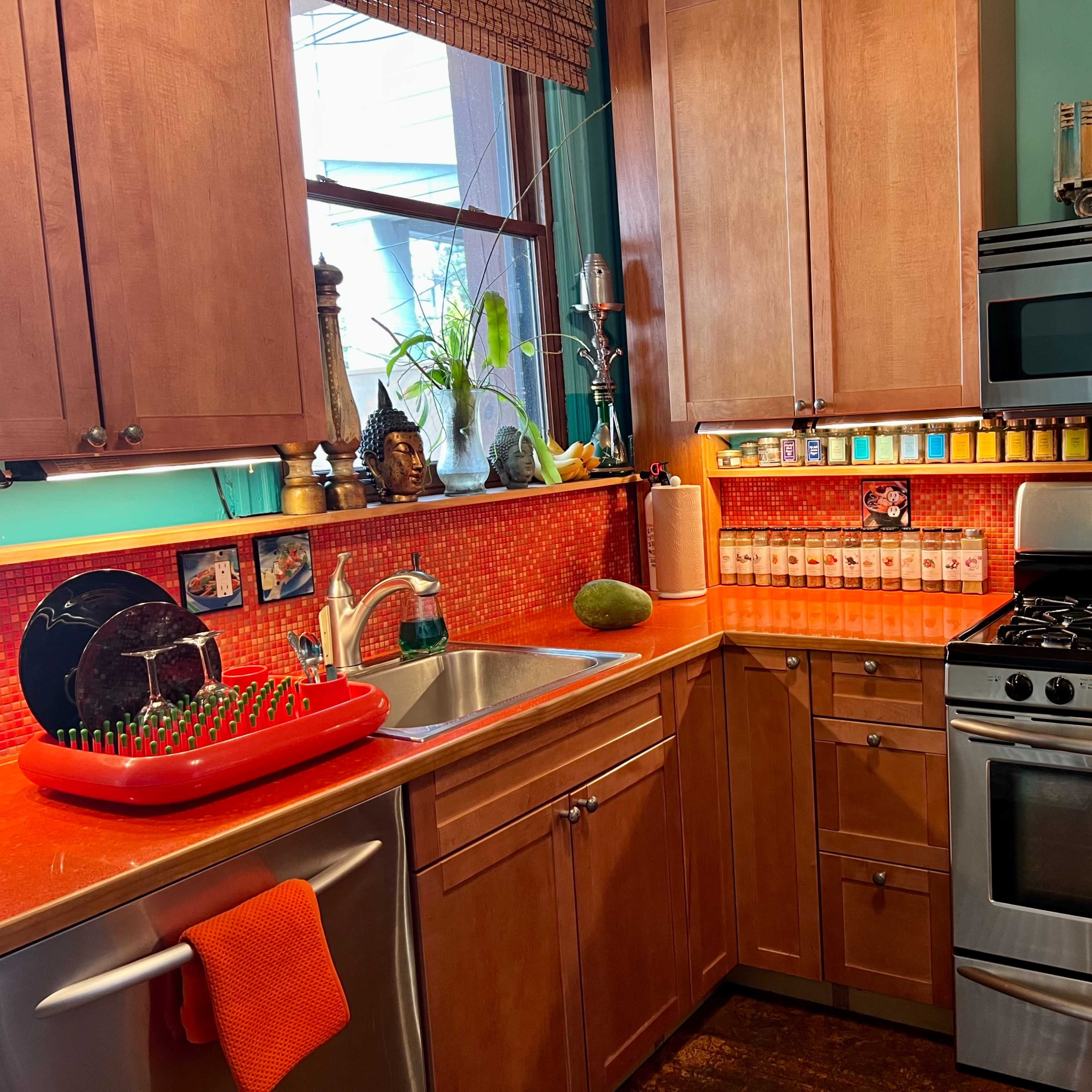 A brightly colored kitchen featuring wooden cabinets, a stainless steel stove, and a sink with a dish rack and decorative items.