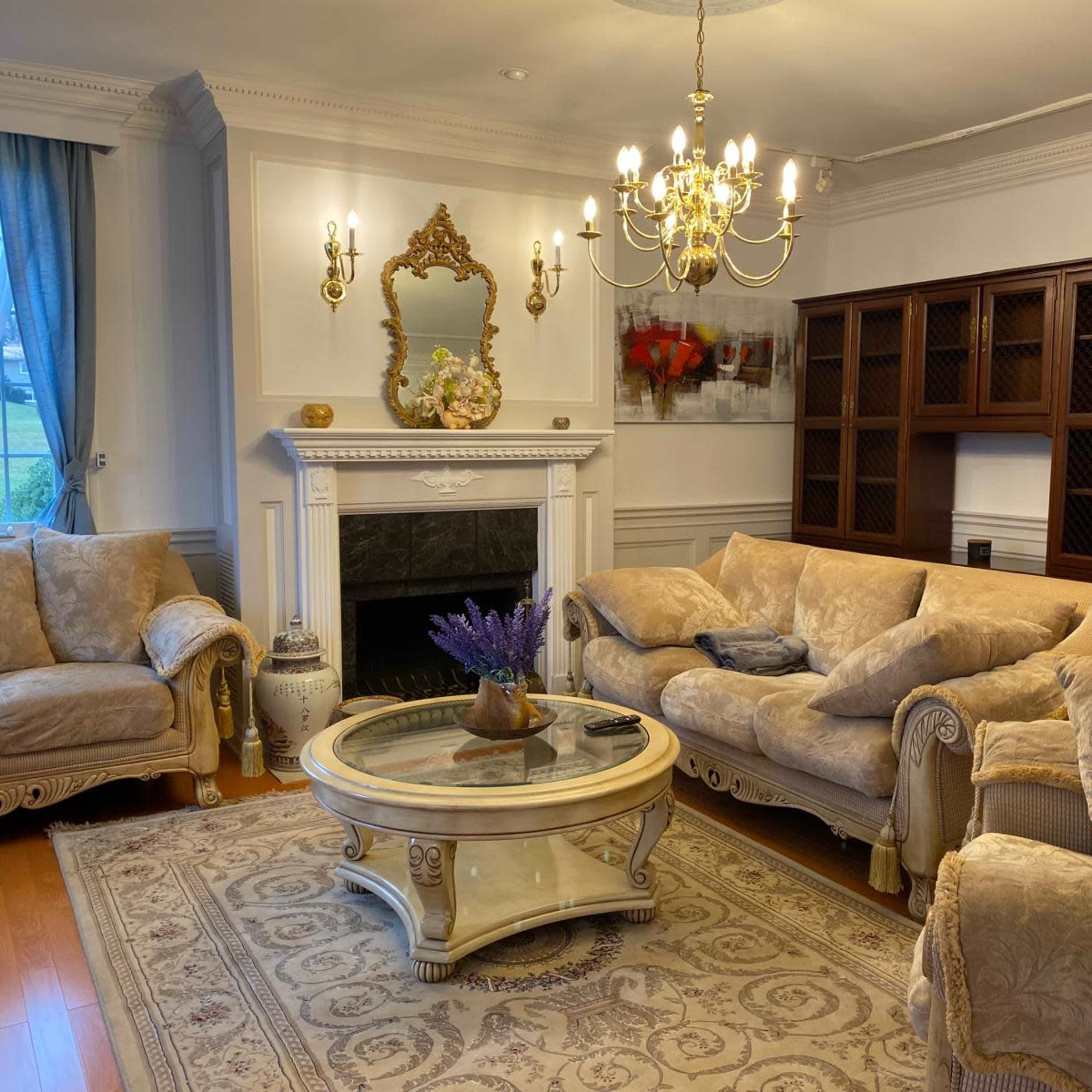 A well-furnished living room features a chandelier, a coffee table with flowers, two sofas, and a bookcase against a wall.