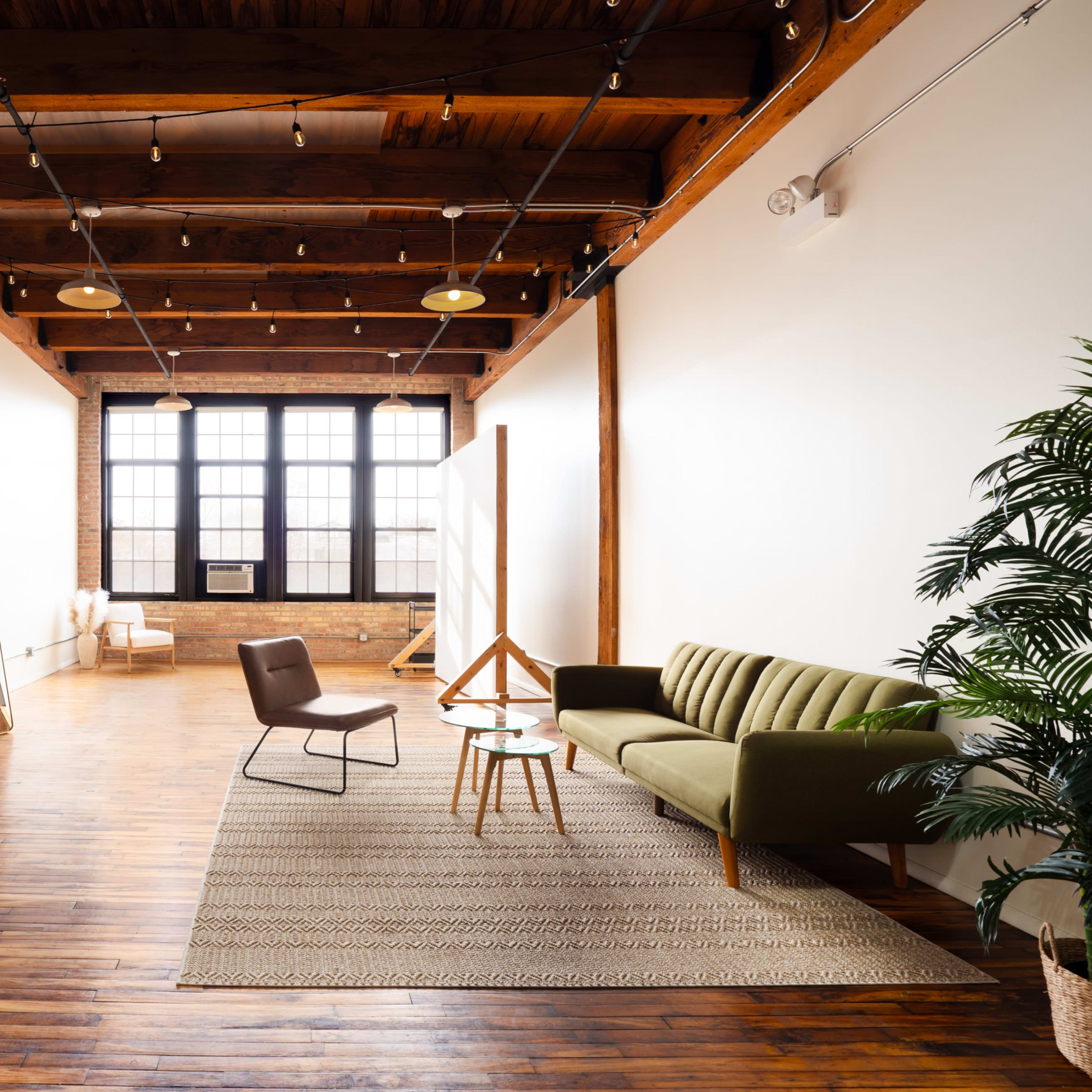 A spacious, modern room featuring wooden beams, a green sofa, a coffee table, and a large window.