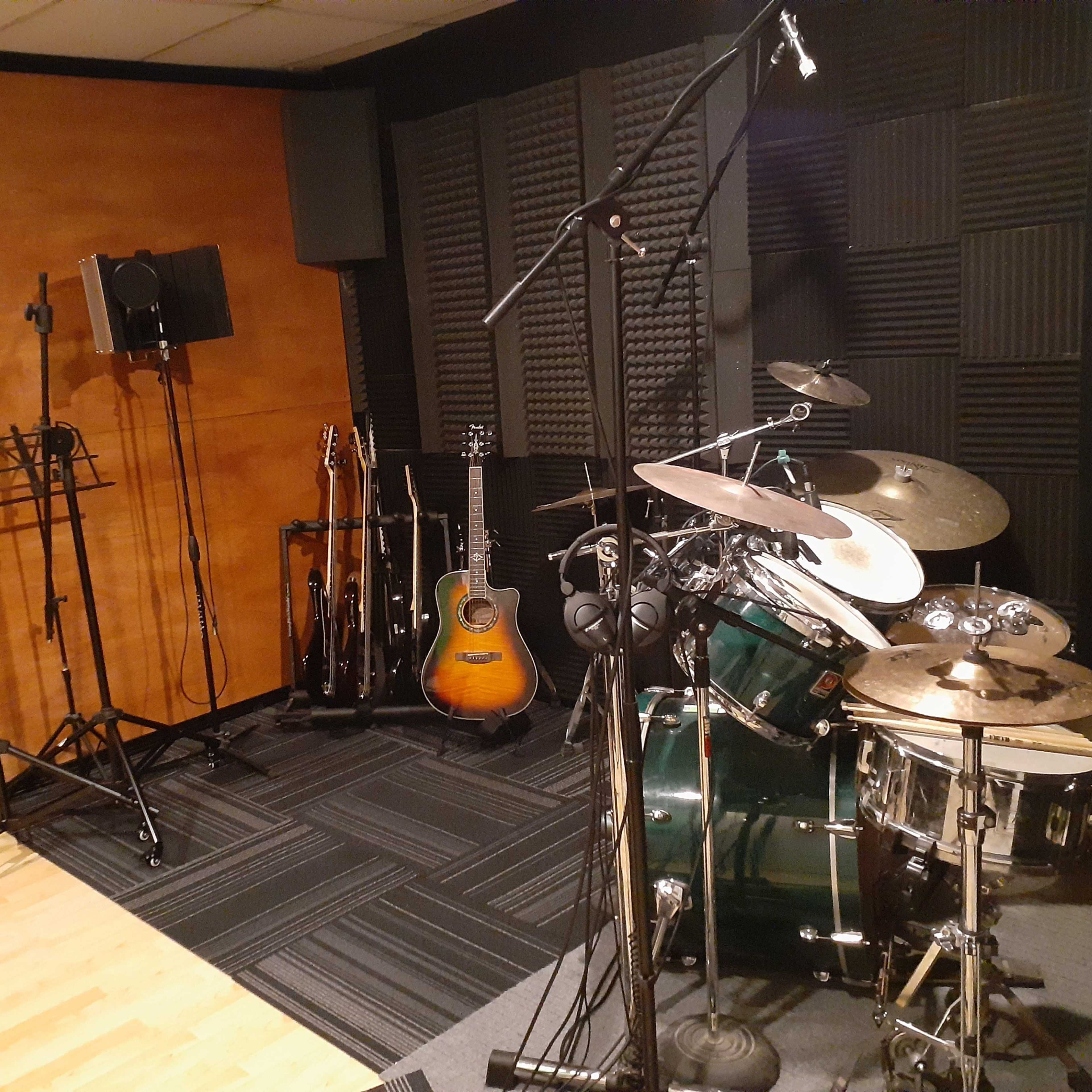 A music recording studio featuring a drum set, several guitars on stands, and soundproofed walls.