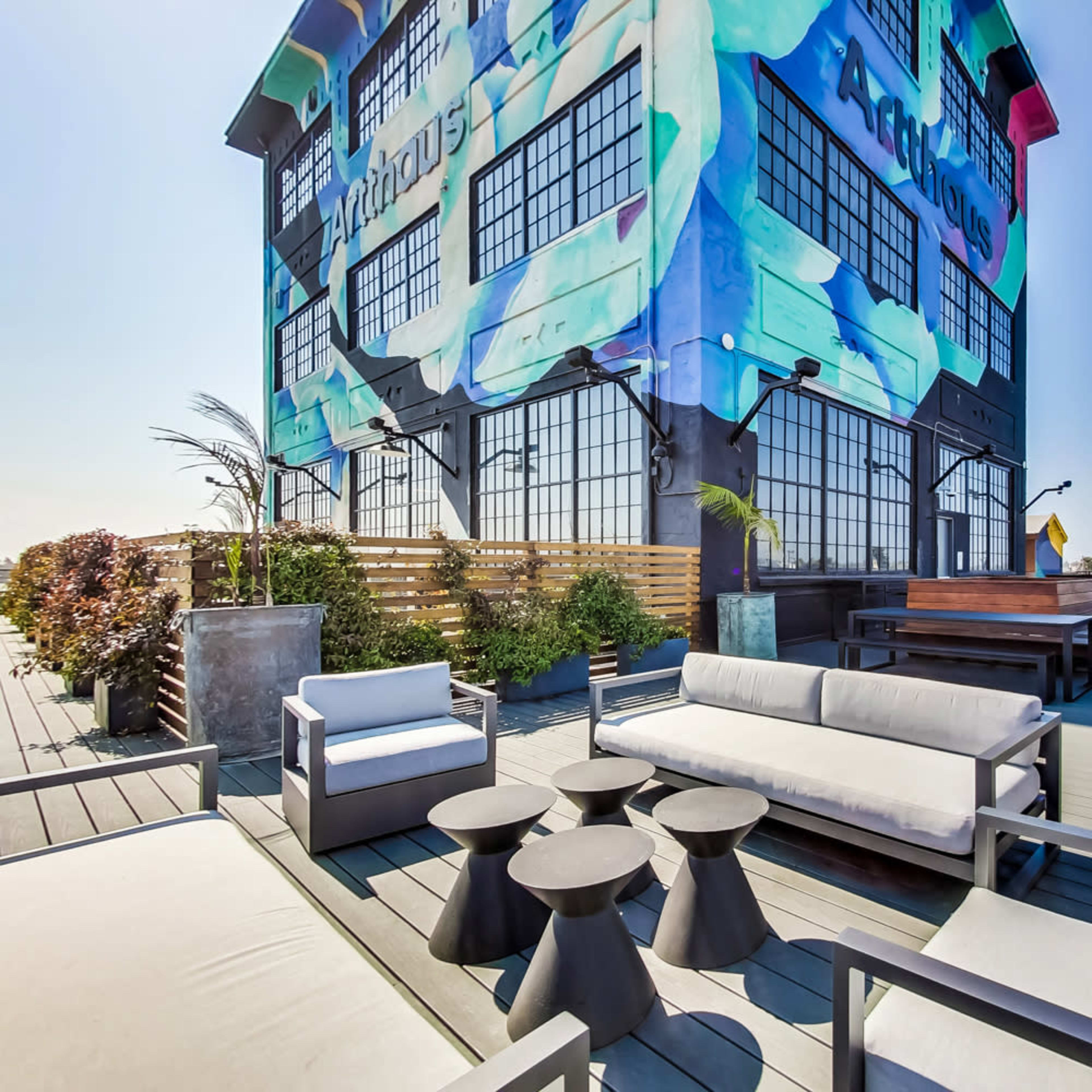 A rooftop terrace featuring modern seating arrangements and a vibrant mural on the side of a building.