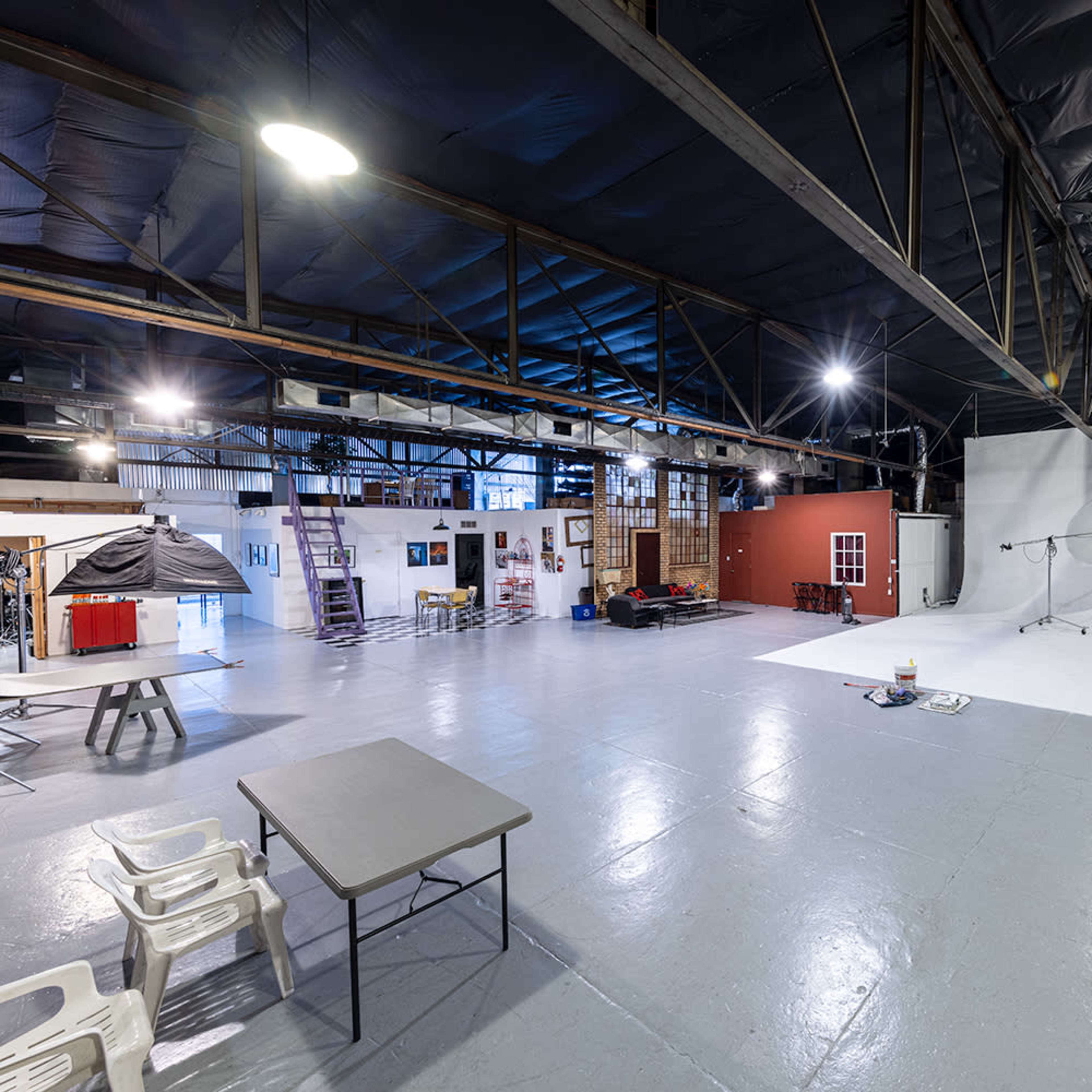 A spacious photography studio with a large white backdrop, various equipment, and multiple seating areas.