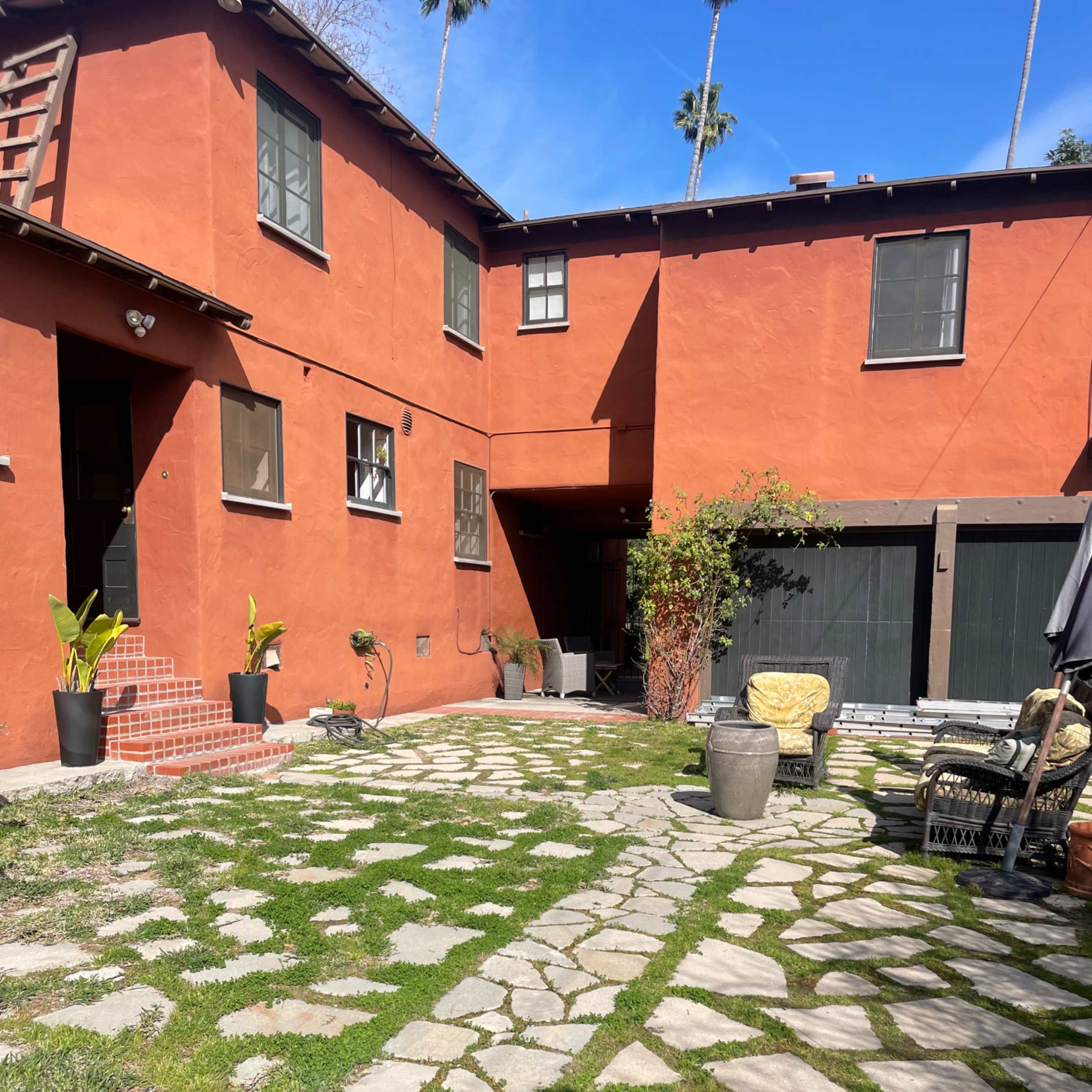 A courtyard with a red-painted building, stone pathways, lush green grass, and potted plants.