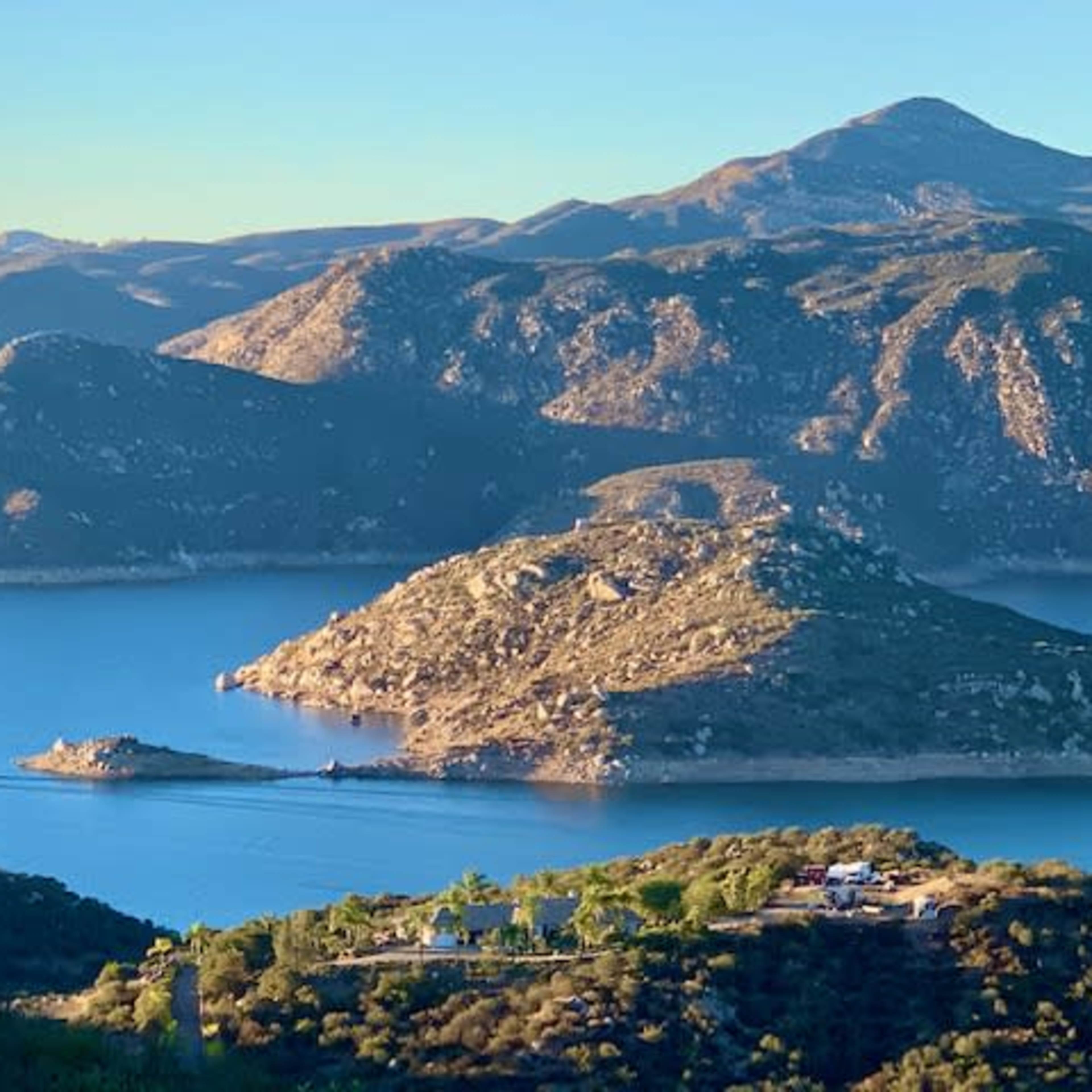 A scenic lake surrounded by hills, with a small island in the center and a boat navigating the water.