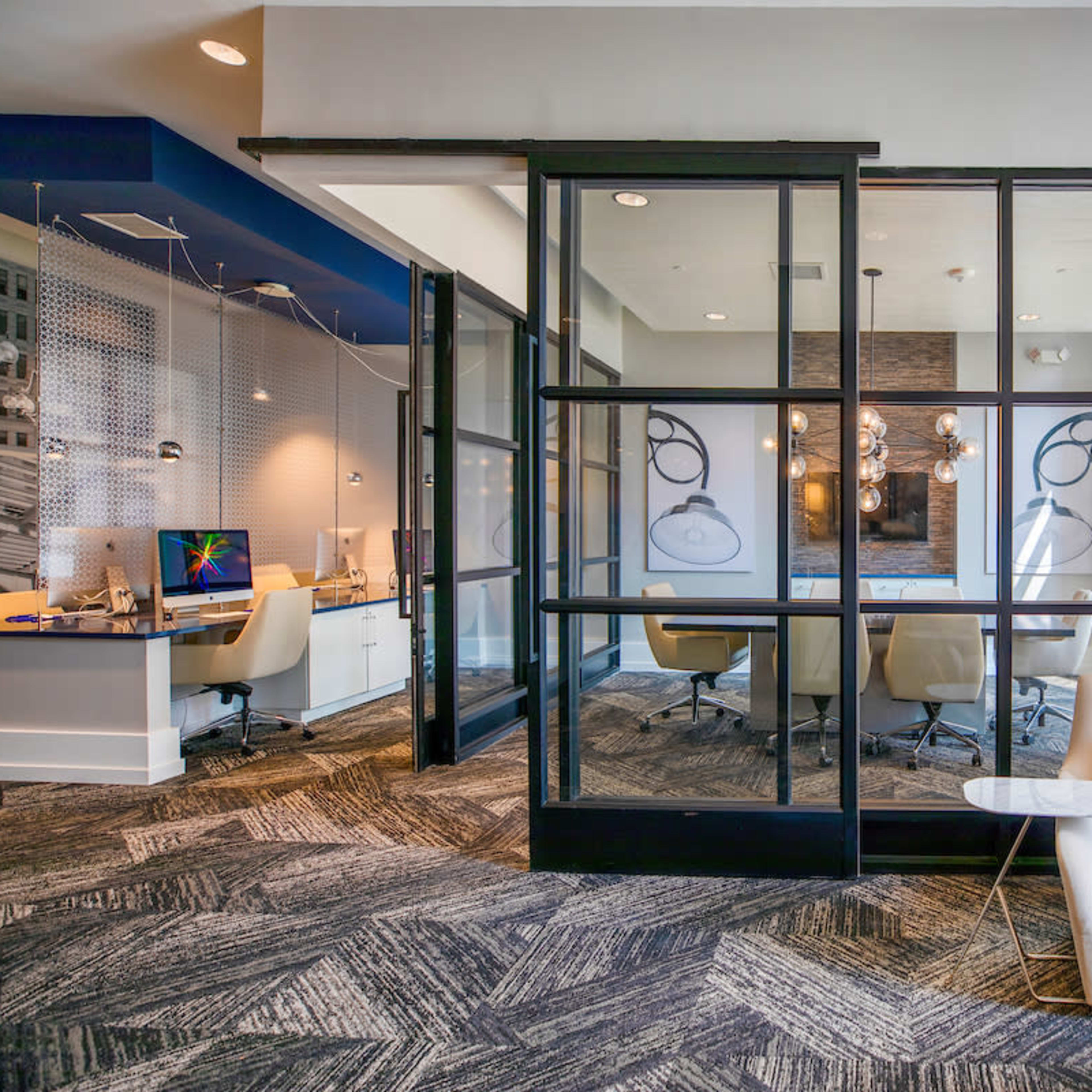 A modern office space with glass-panelled doors leading to a conference room, featuring contemporary furniture and a patterned carpet.