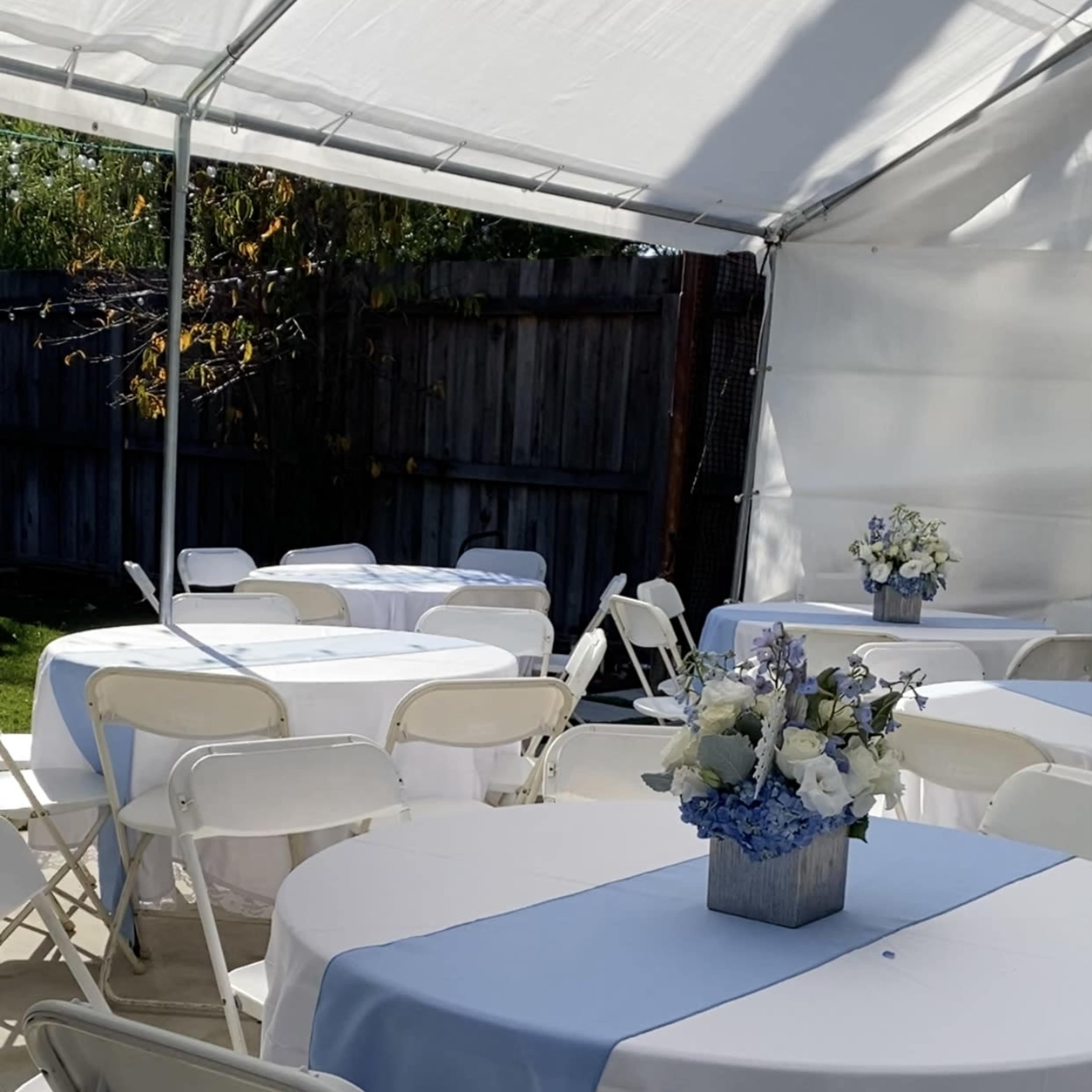 A tented area features several tables covered with white and blue linens, arranged with floral centerpieces.