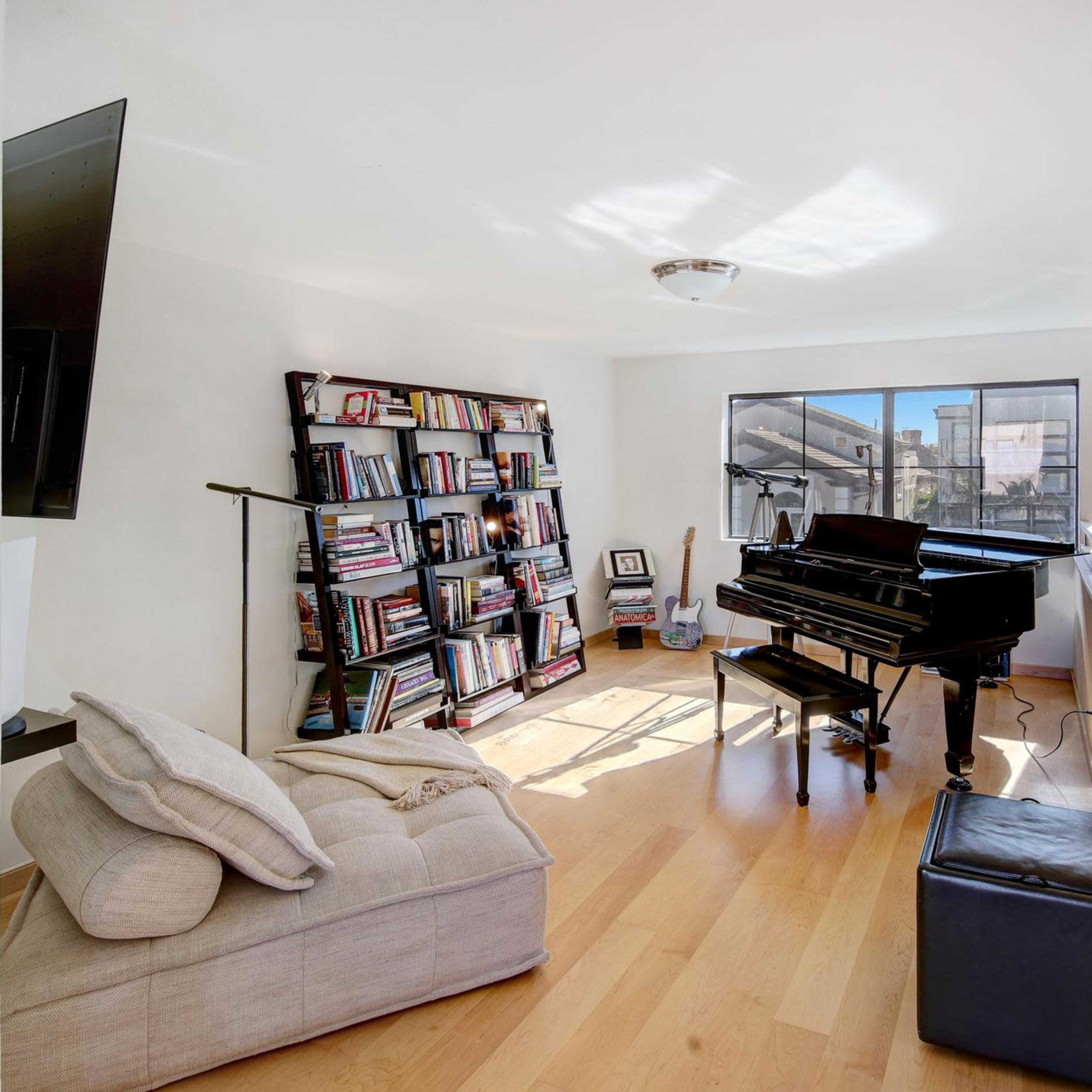 A modern room featuring a black piano, a bookshelf filled with books, and large windows allowing natural light to enter.