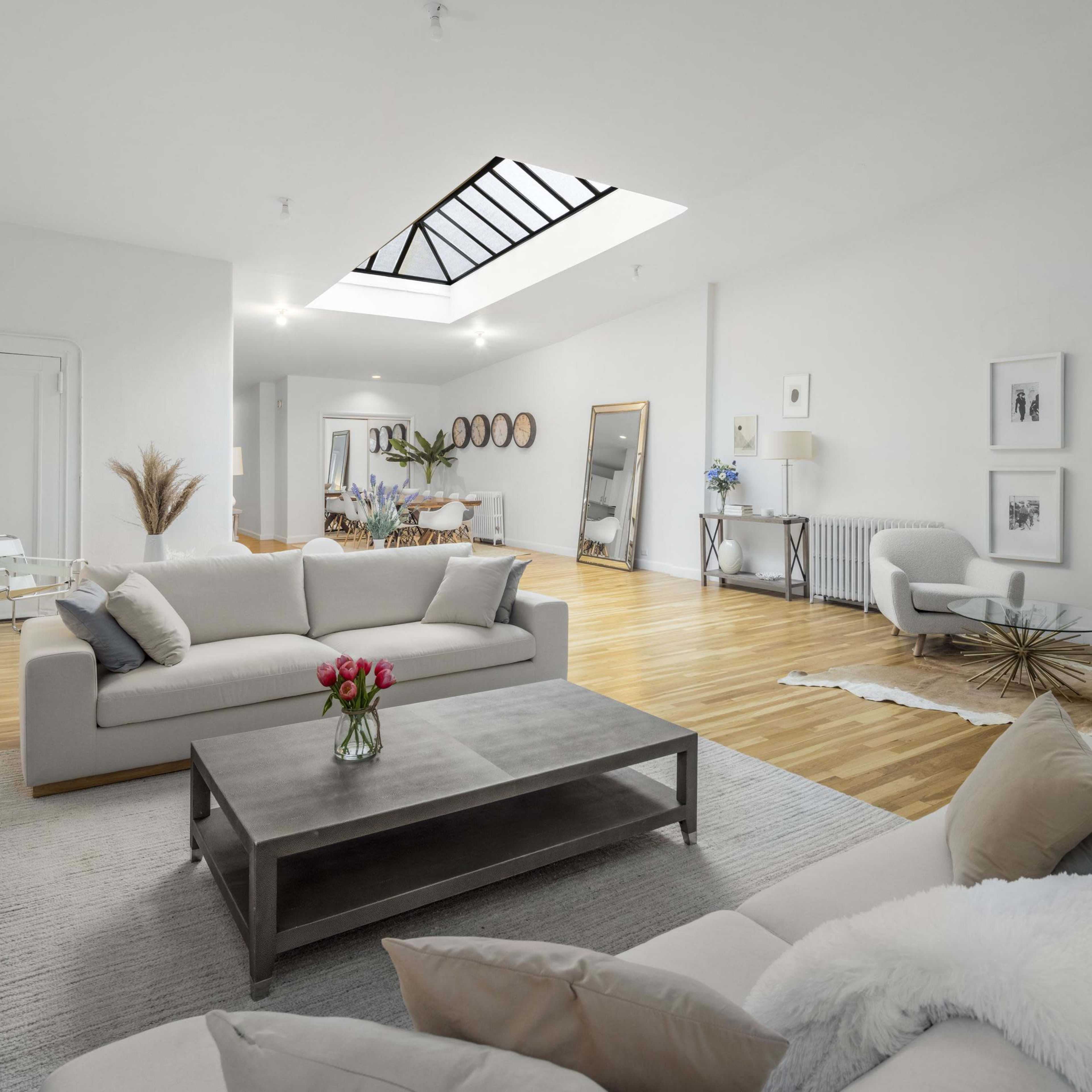 The spacious living area features a modern design with a large sofa, minimalist furniture, and natural light streaming through a skylight.