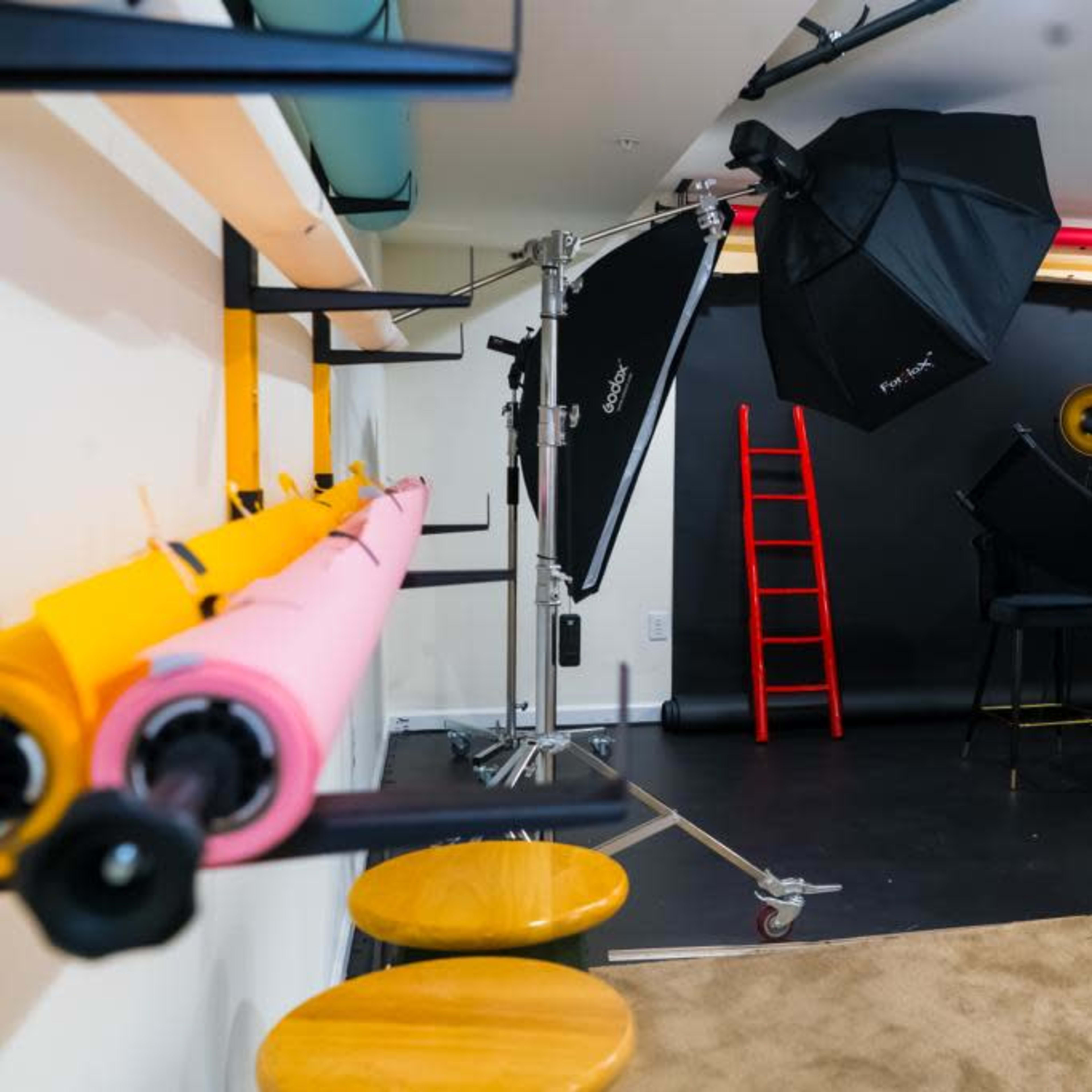 A photography studio setup, featuring backdrops, lighting equipment, a ladder, and a camera on a tripod.
