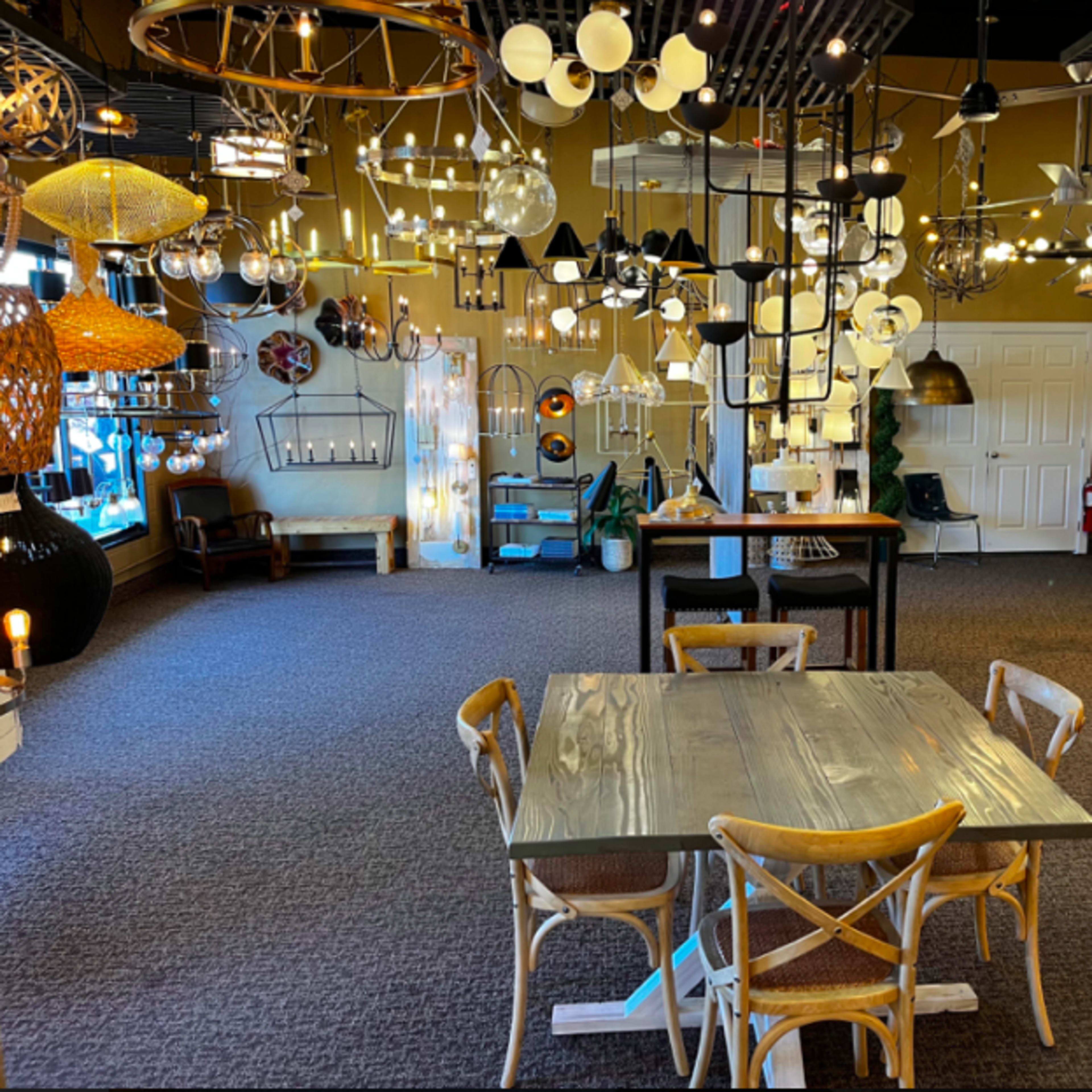 A showroom filled with various lighting fixtures and furniture, featuring a central table surrounded by chairs.