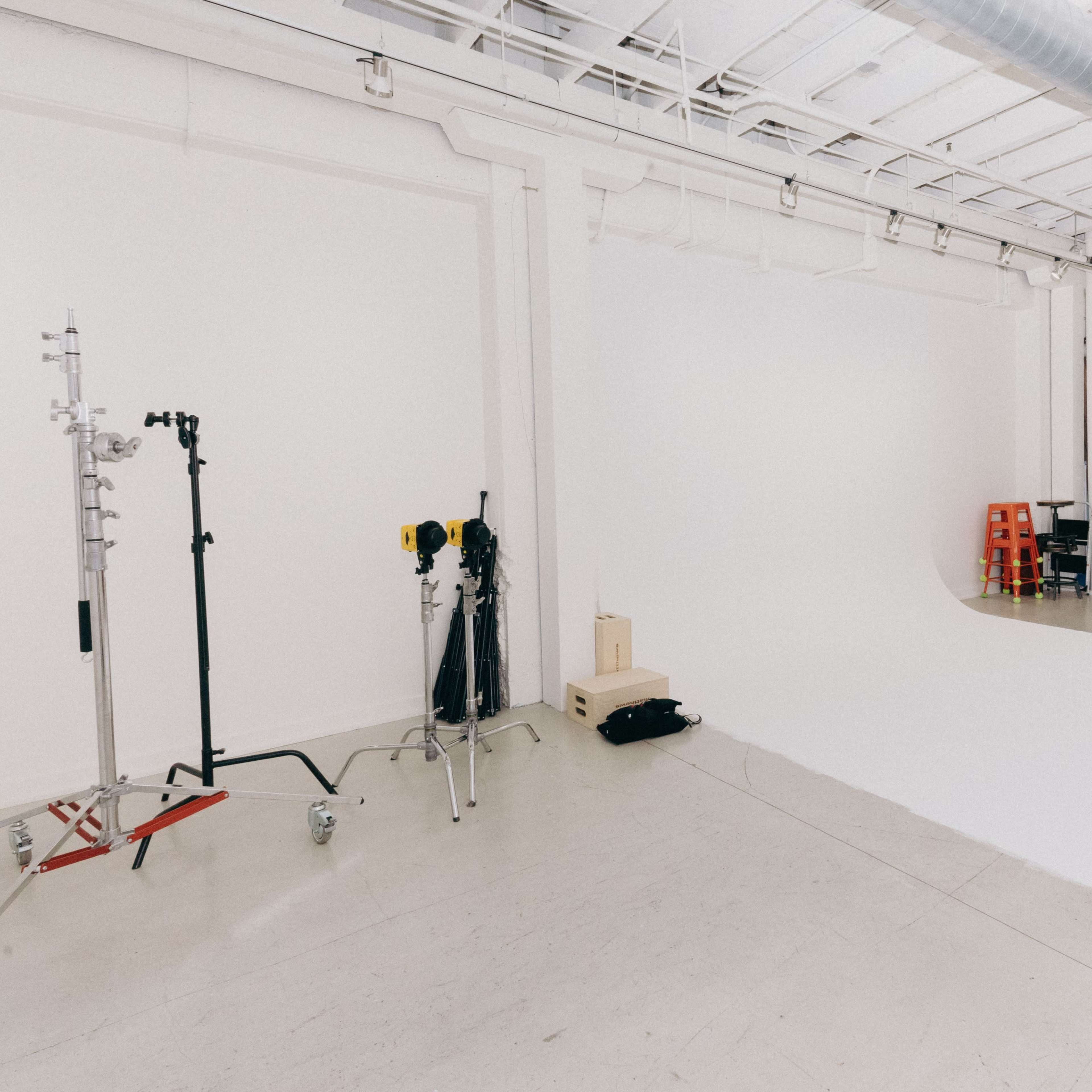 A minimalist photo studio with white walls, a roll of white backdrop material, and a couch next to a door.