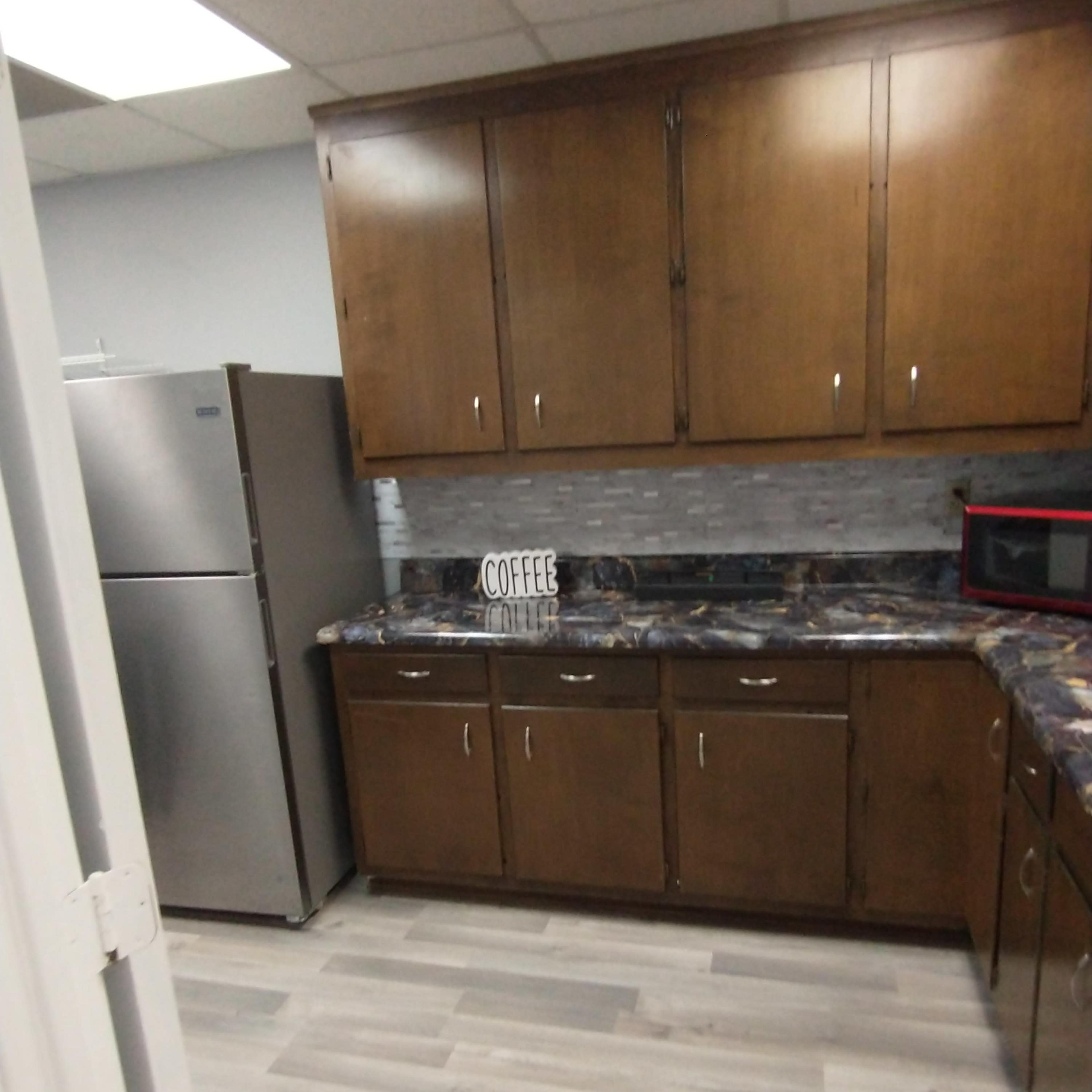 A modern kitchen featuring wood cabinetry, a stainless steel refrigerator, and a countertop with a coffee-themed decor item.