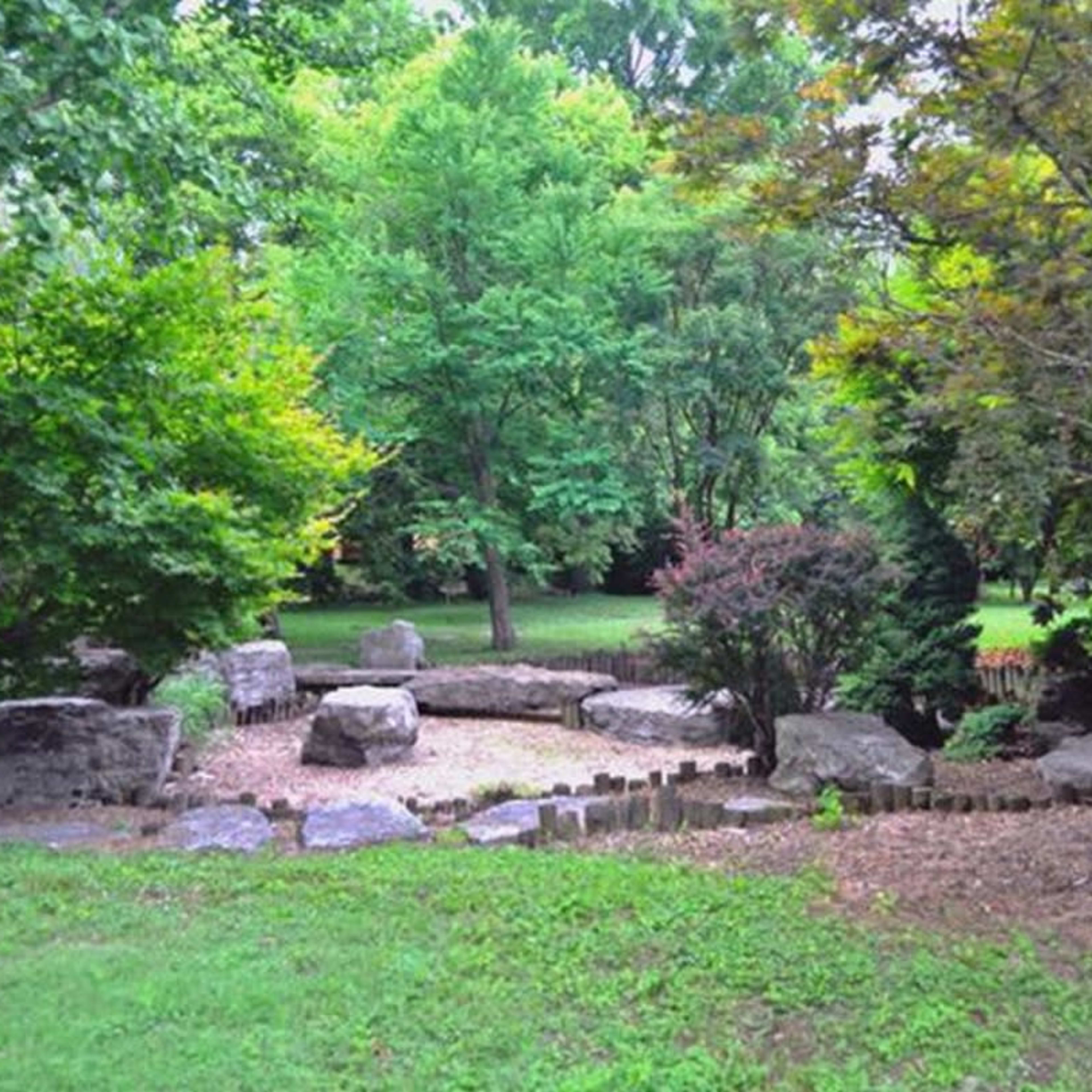 A serene garden features a clearing surrounded by trees and large rocks.