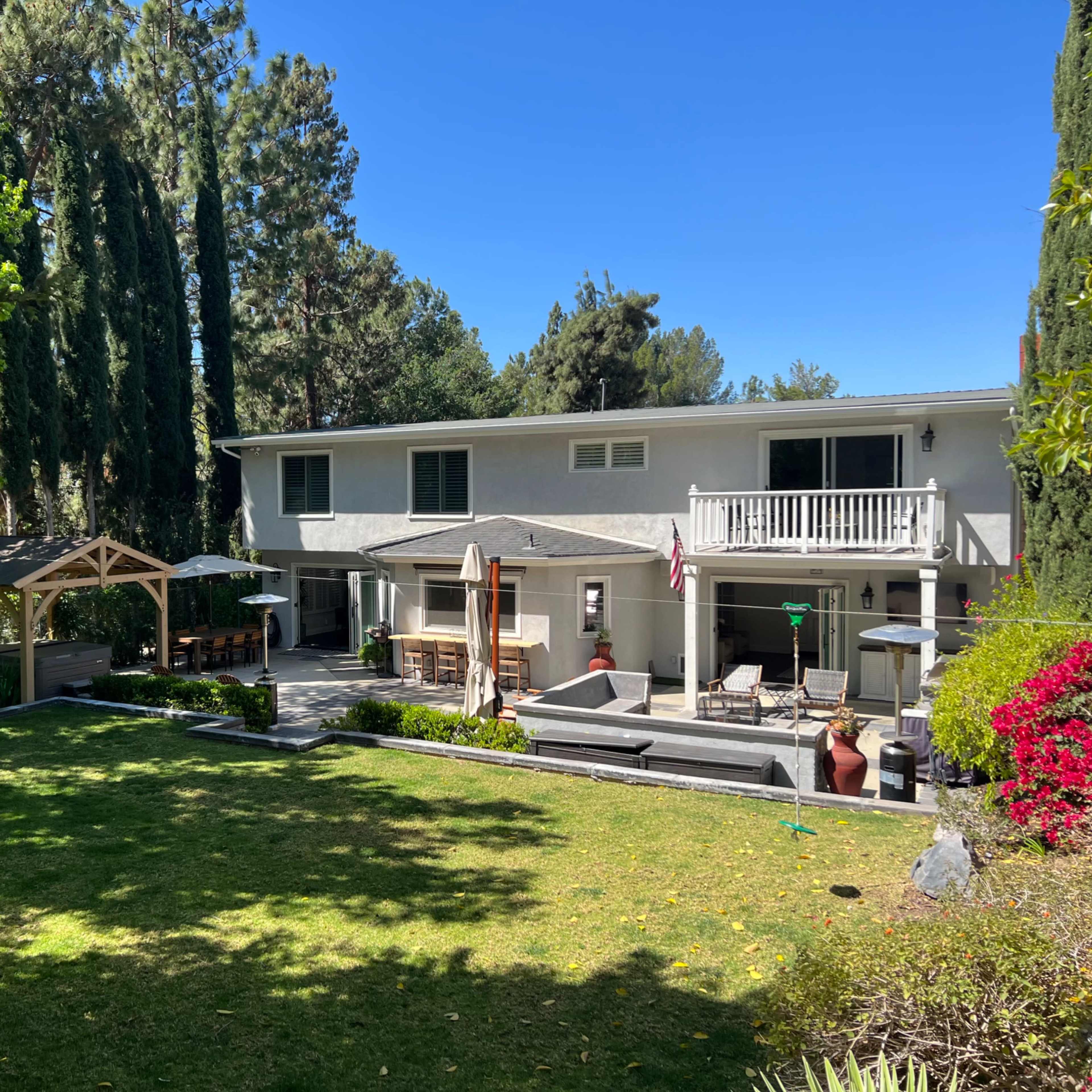 A two-story house with a patio, surrounded by a lawn and trees in a landscaped yard.