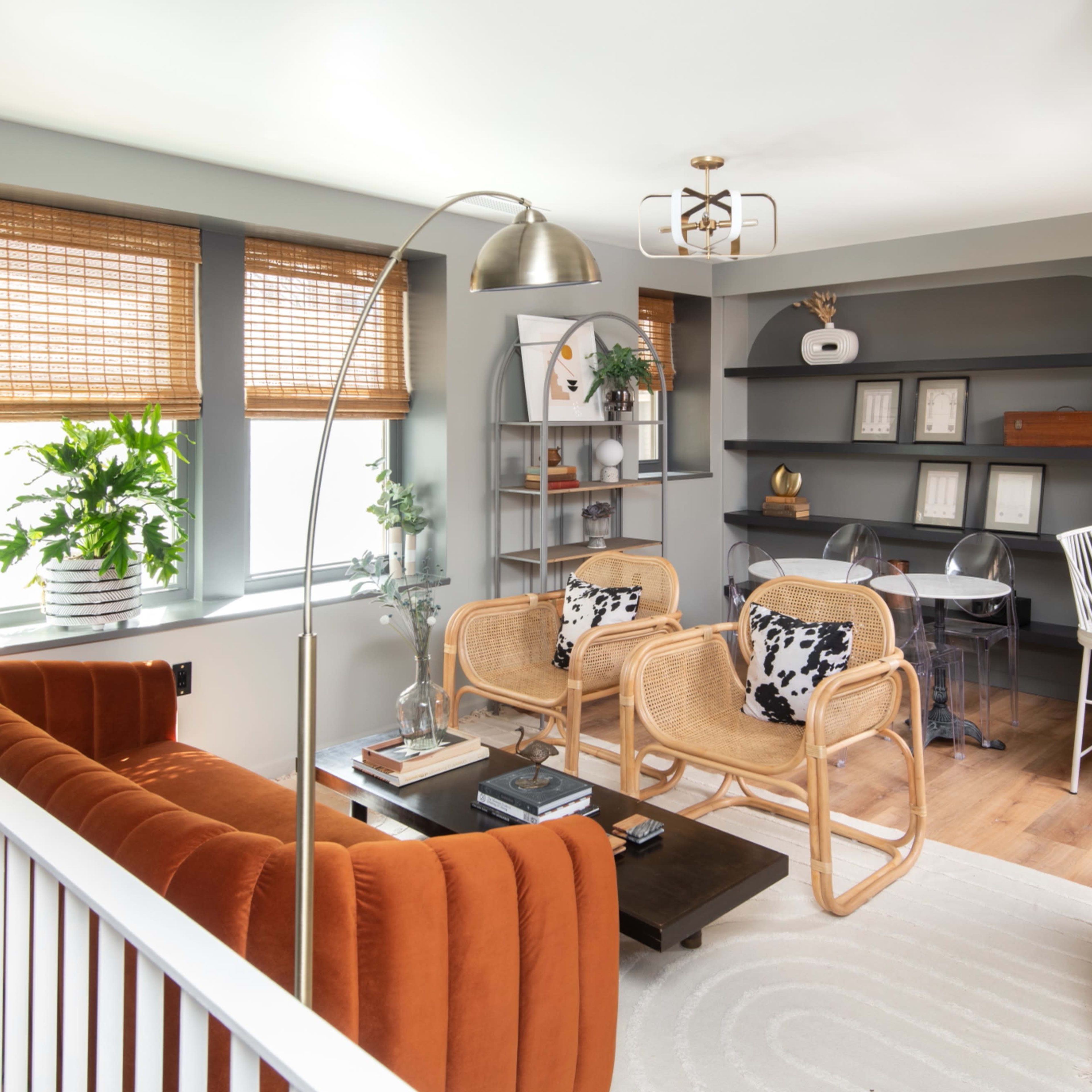 A modern living room with a rust-colored sofa, two rattan chairs, a coffee table, and shelves displaying decor and framed pictures.