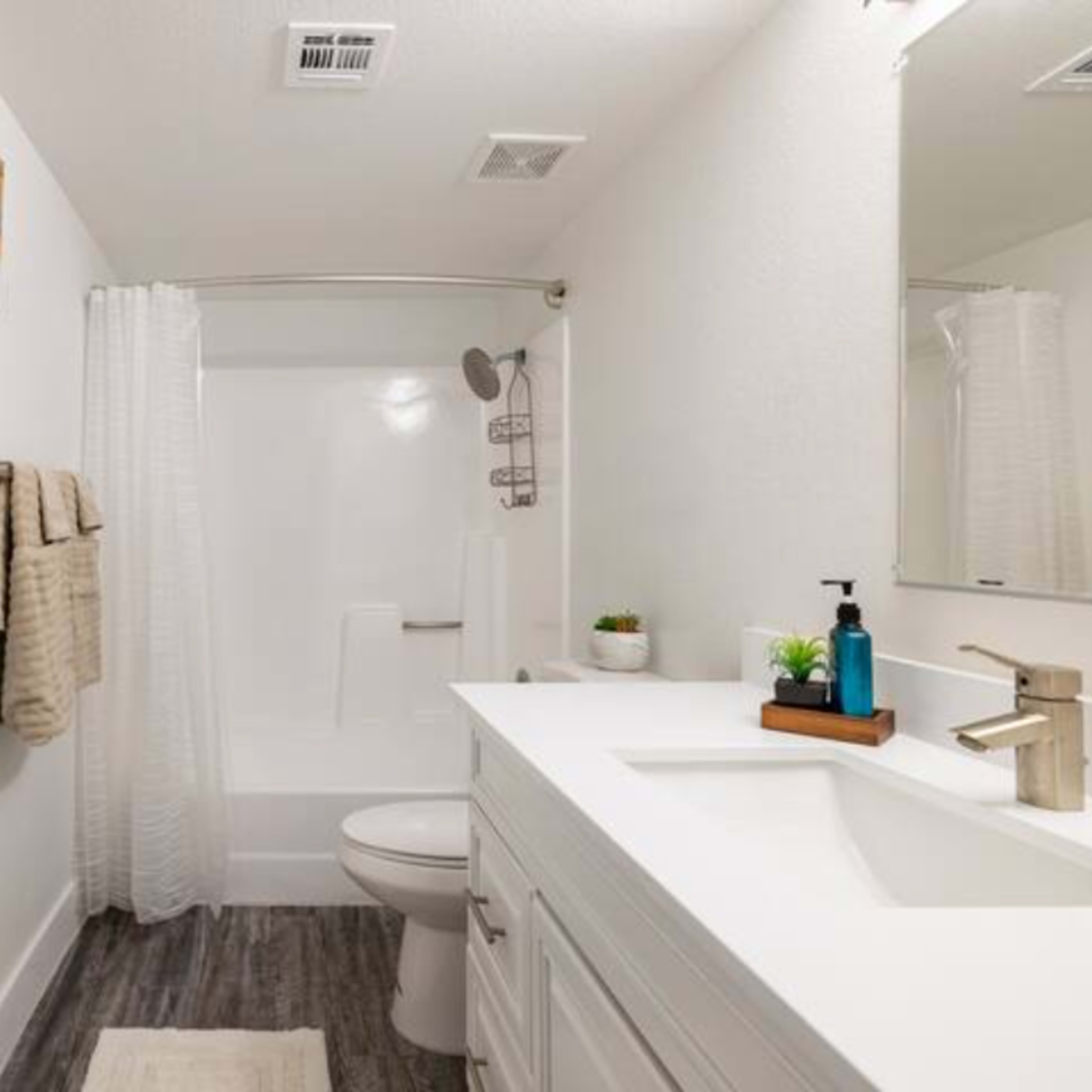 A clean, modern bathroom featuring a bathtub with a shower, a white vanity with a sink, and light-colored walls.