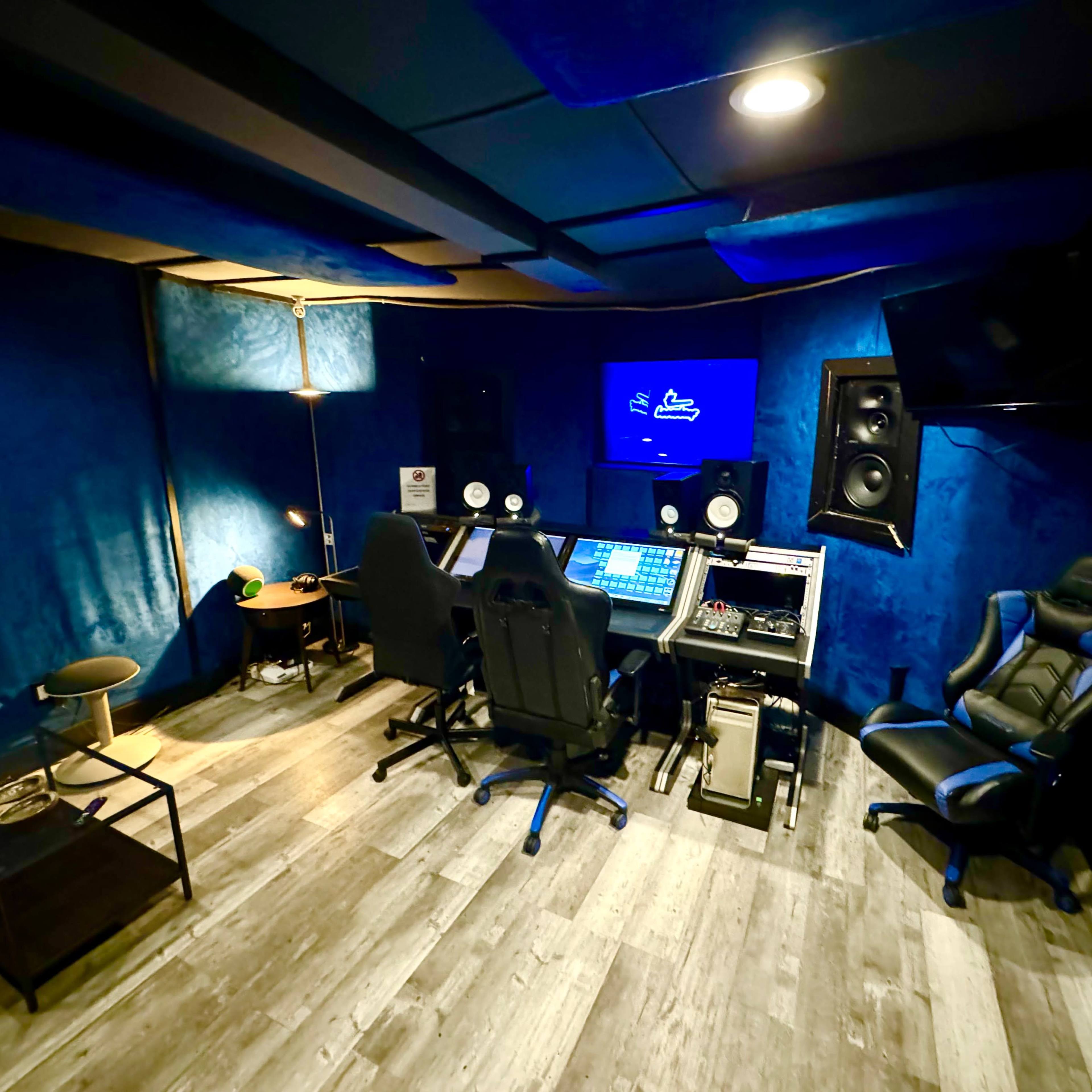 A soundproof music studio featuring a control station with audio equipment, two chairs, and blue acoustic panels on the walls.