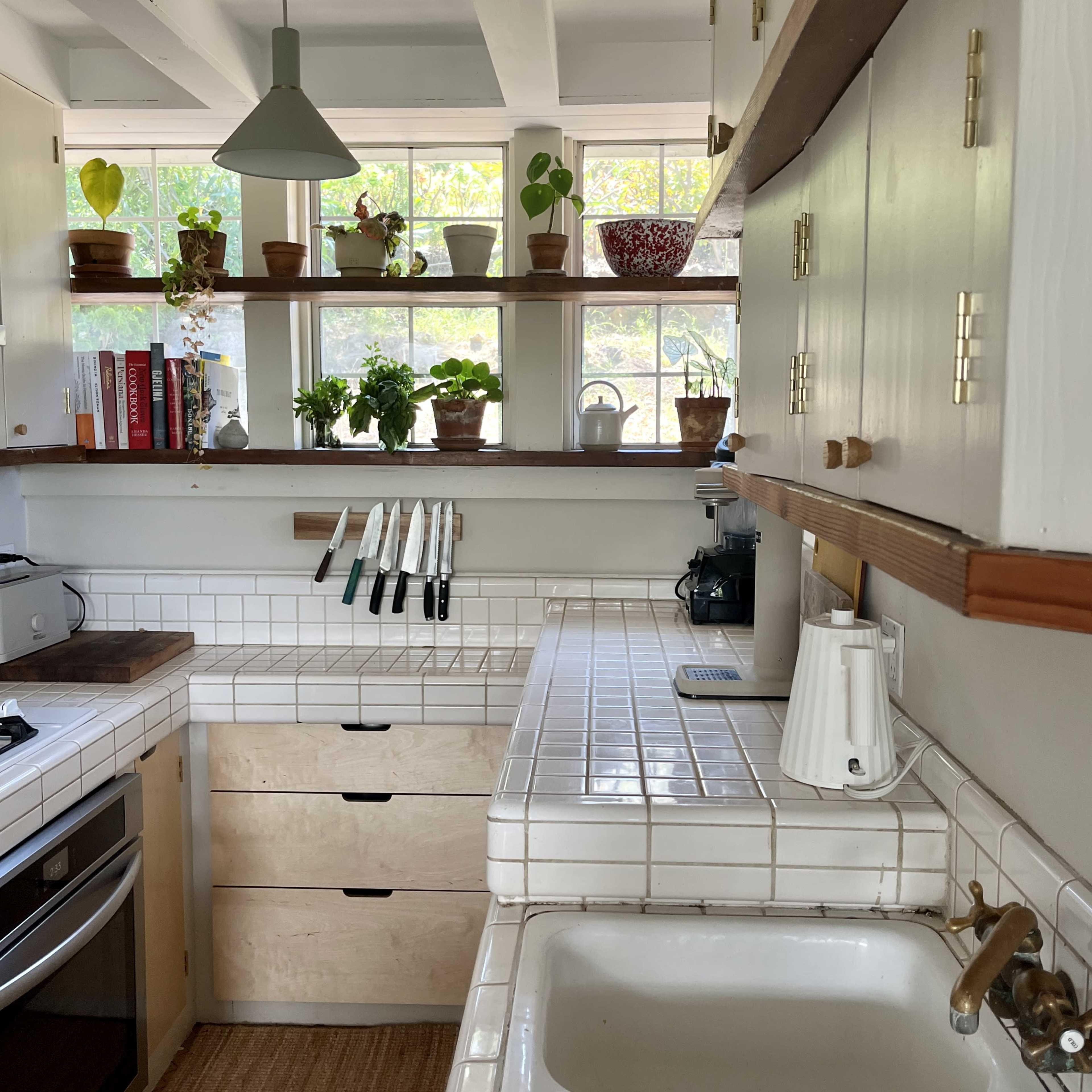 A kitchen with wooden shelves displaying potted plants and kitchen utensils, along with a sink and a stove built into the cabinetry.