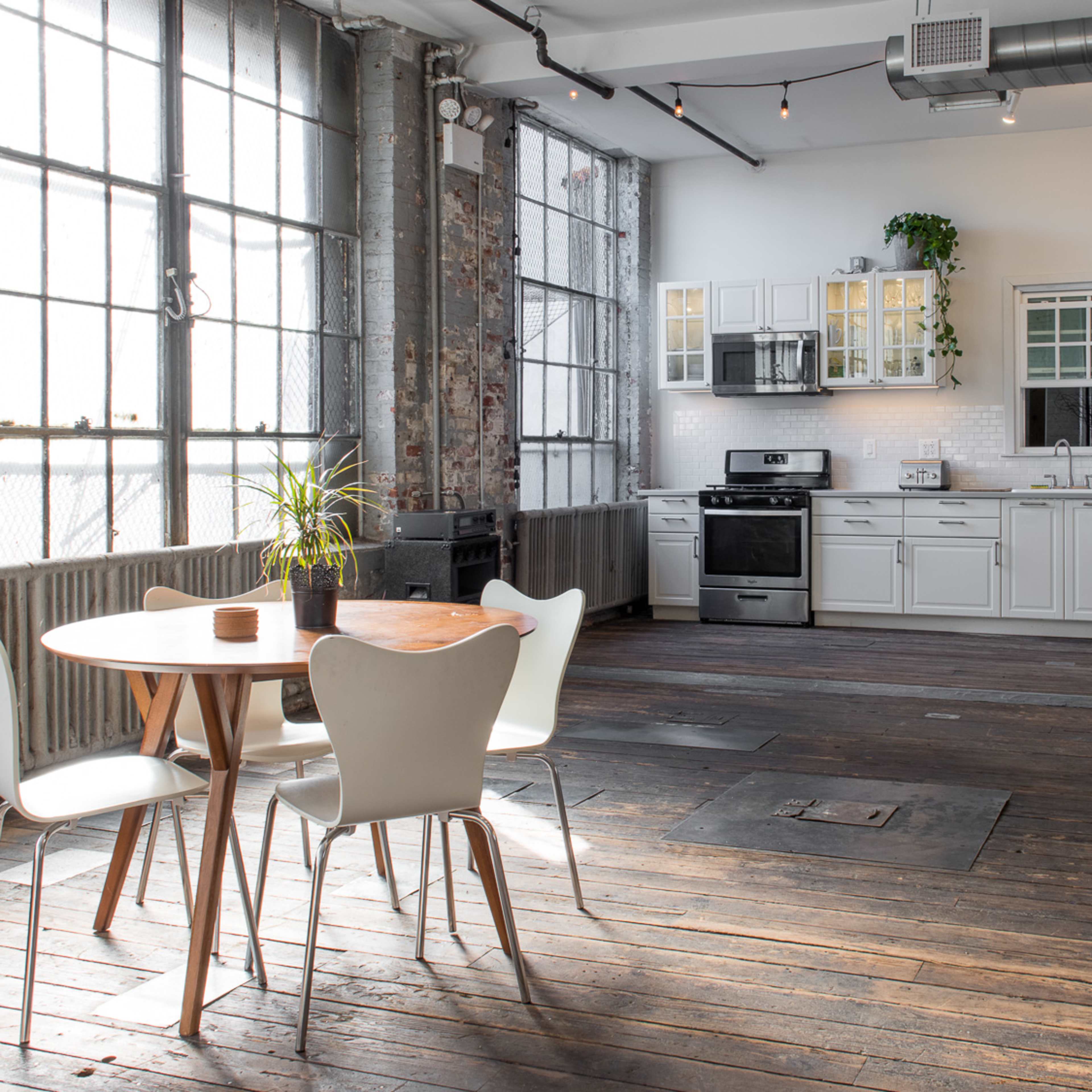 A modern kitchen features white cabinets, stainless steel appliances, and a small dining area with a round wooden table and white chairs.