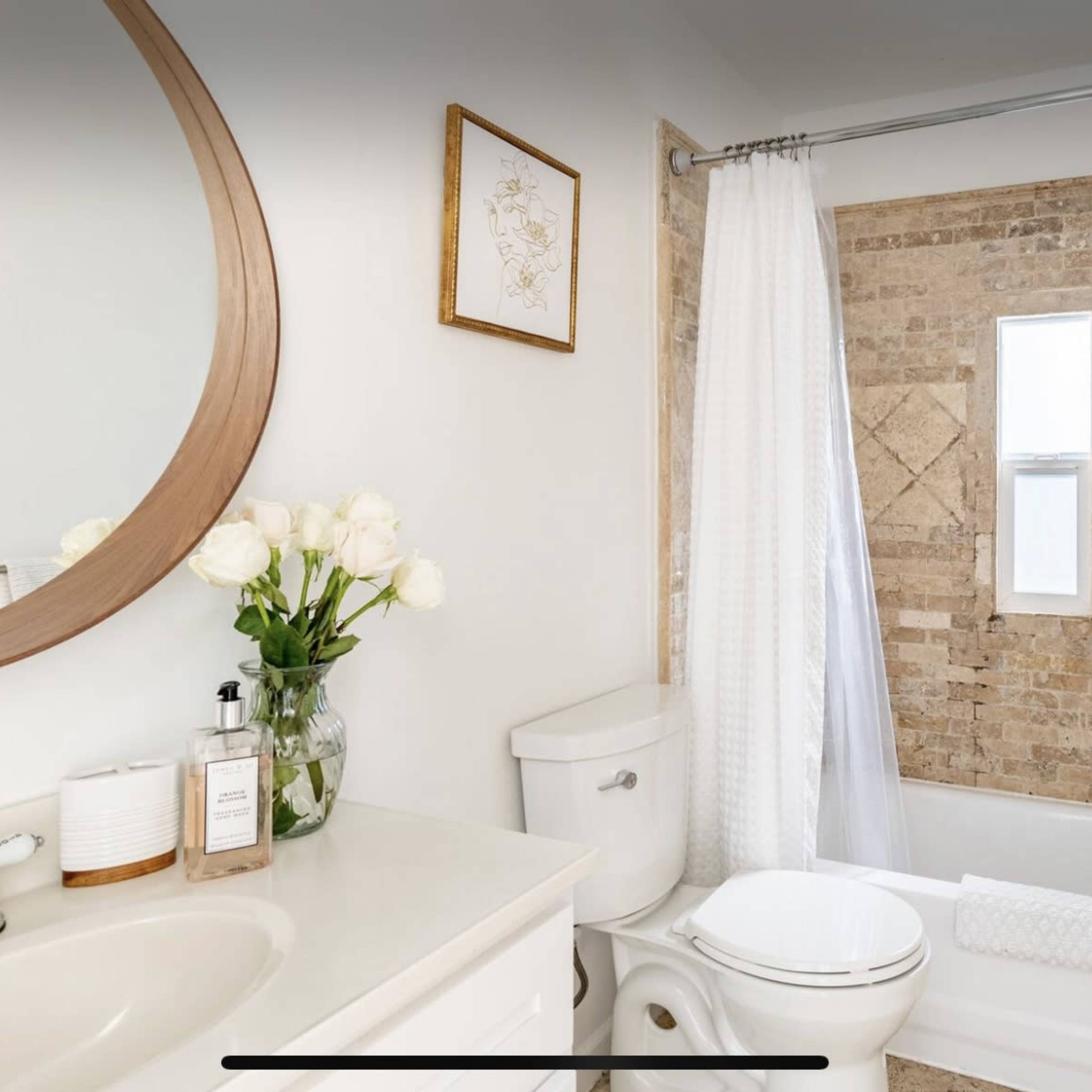 A modern bathroom featuring a white sink and toilet, a bathtub with a shower, and a window surrounded by tiled walls.
