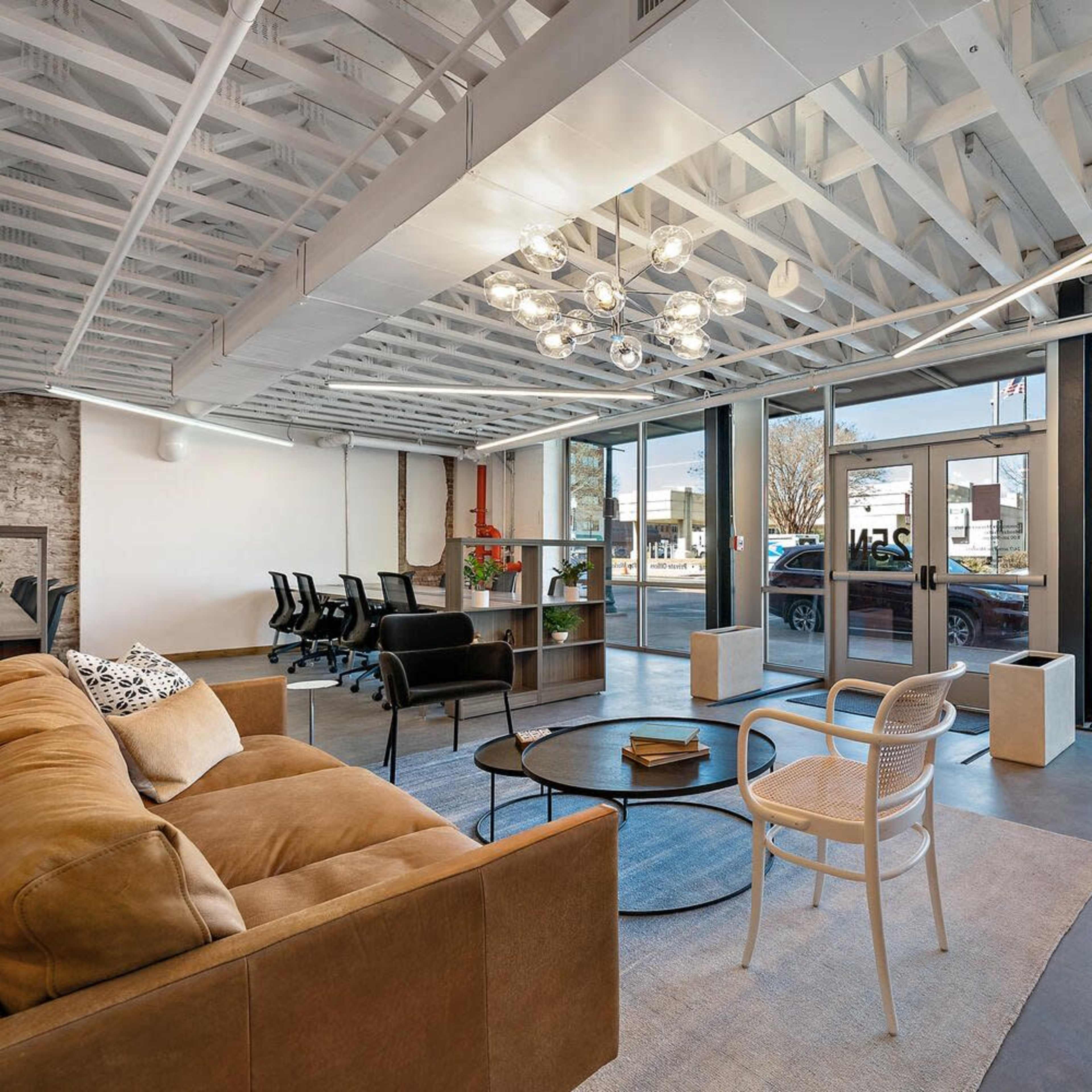 A modern office space with a sectional sofa, a round coffee table, and large windows facing the street.