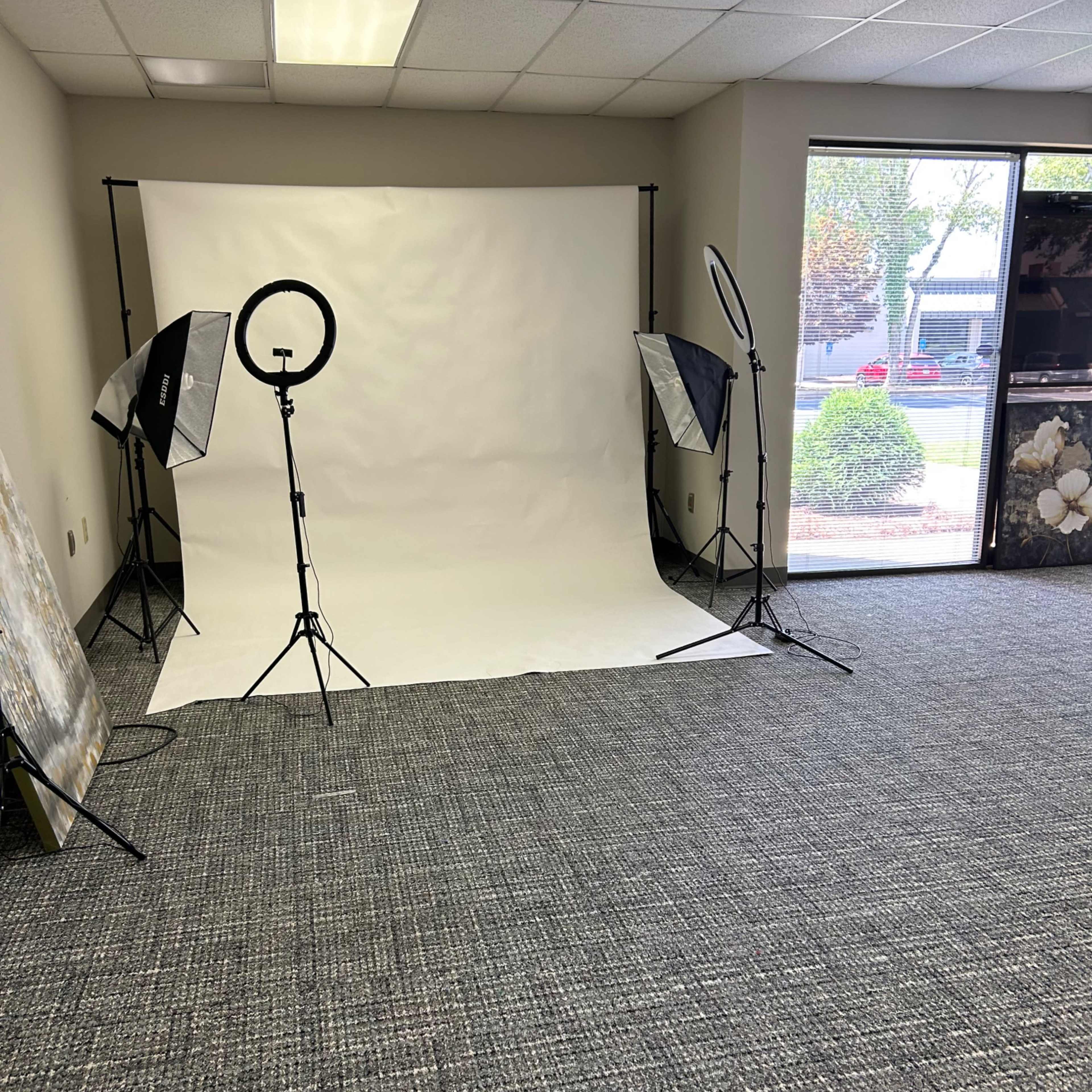 A photography studio setup with a white backdrop, lighting equipment, and a carpeted floor.