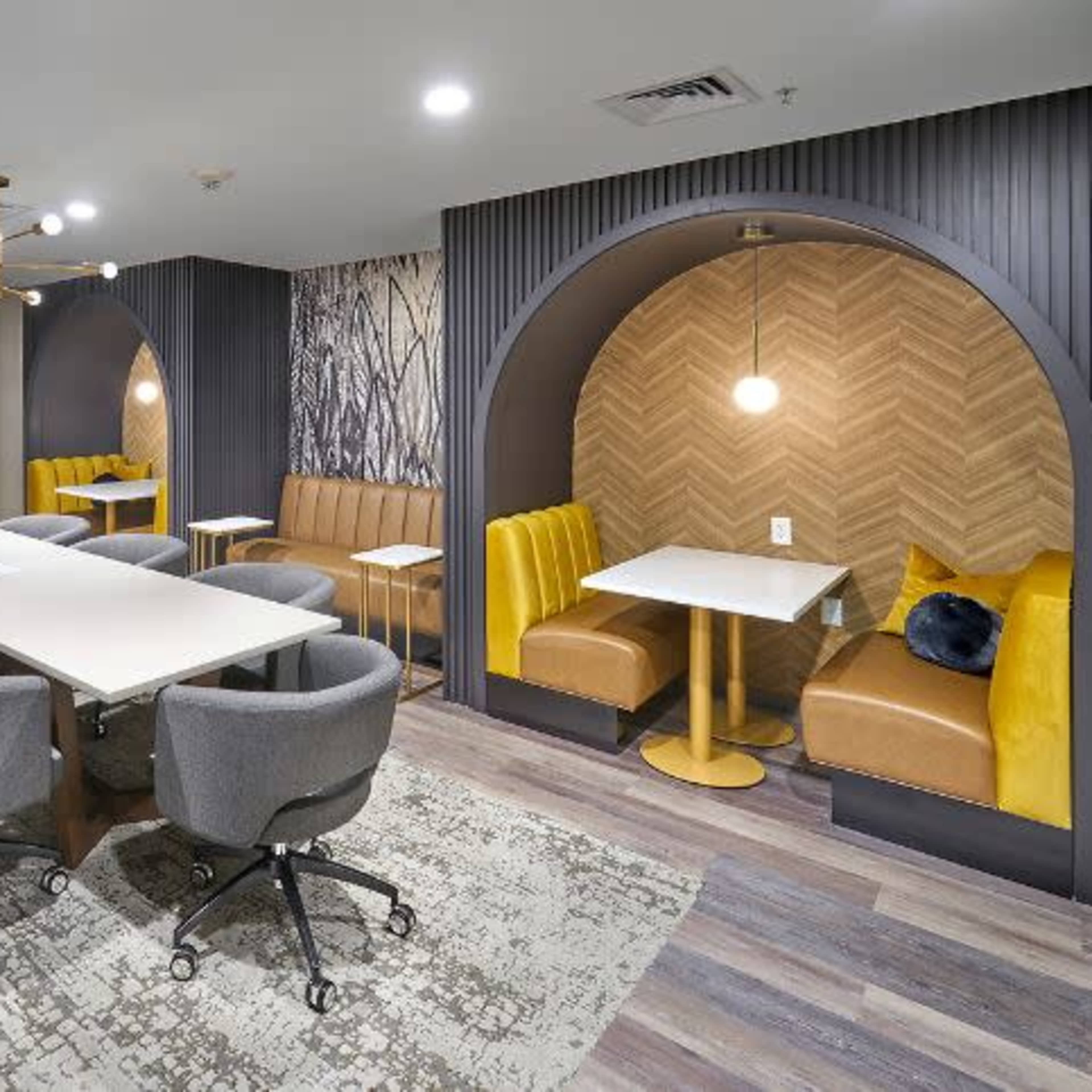 A modern meeting room with a large table surrounded by swivel chairs, accompanied by cozy booths with warm yellow upholstery and decorative lighting.
