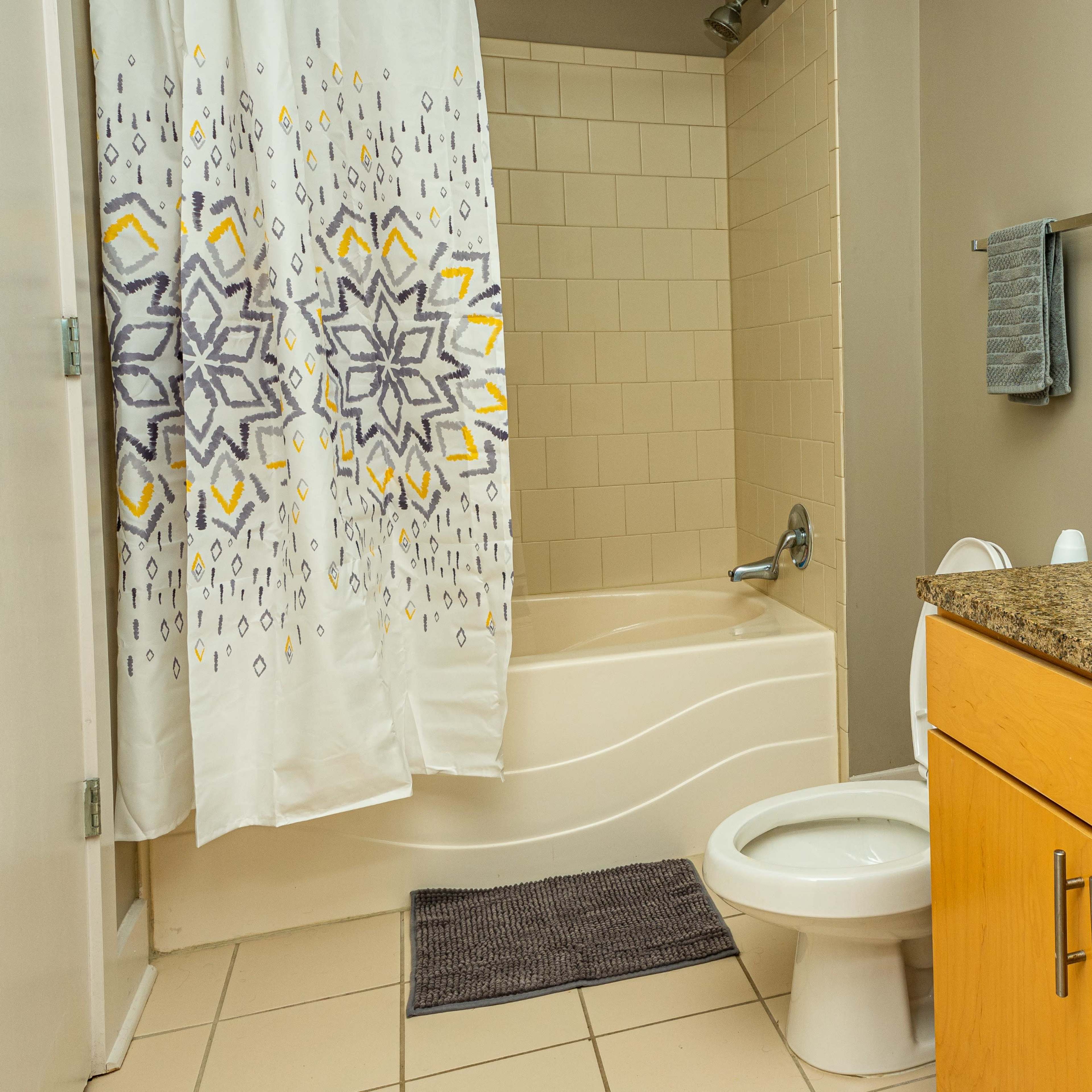 A bathroom featuring a bathtub with a shower curtain, a toilet, and a countertop with a sink and mirror.