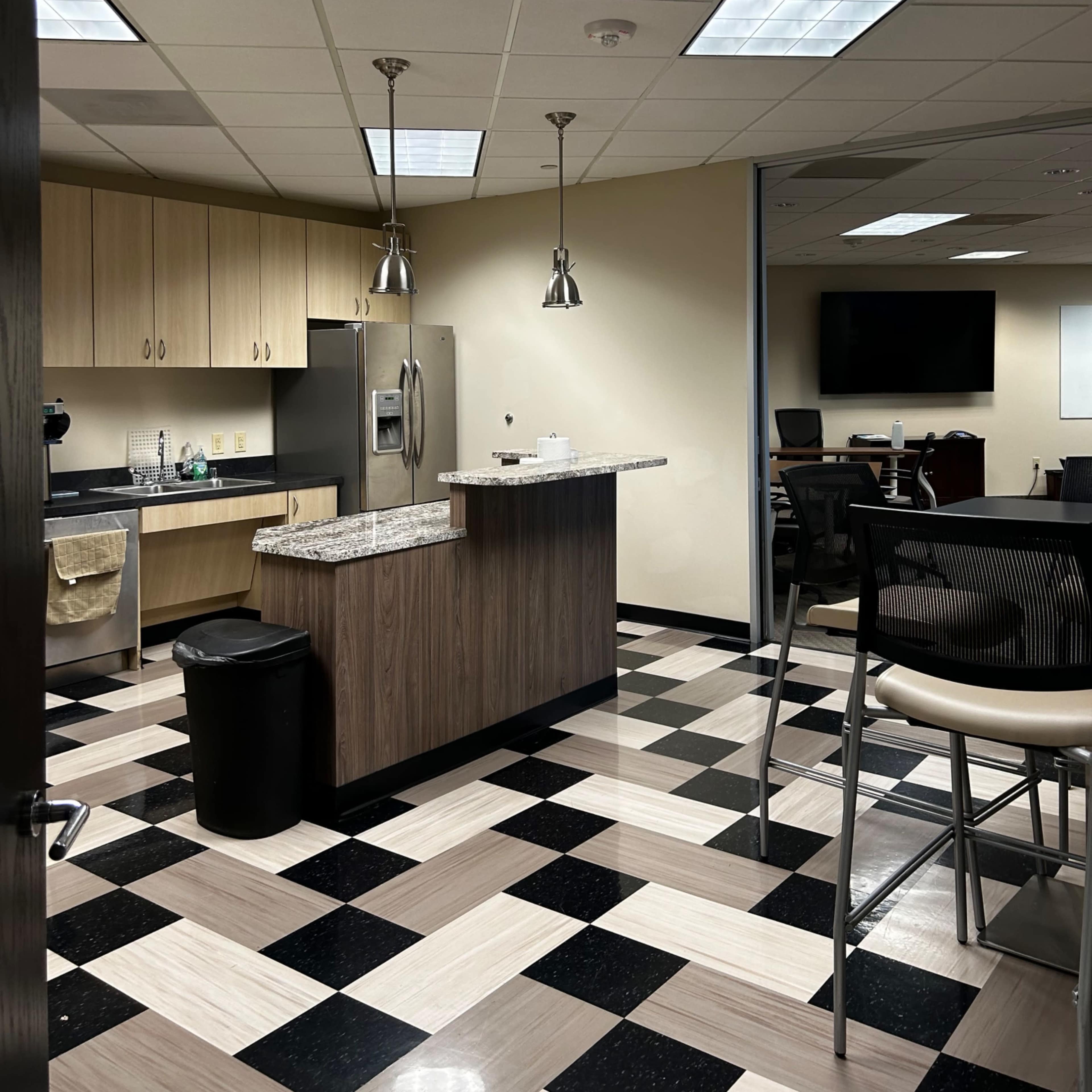 A modern kitchen area with a granite countertop, stainless steel appliances, and a checkered floor in a multi-purpose office space.