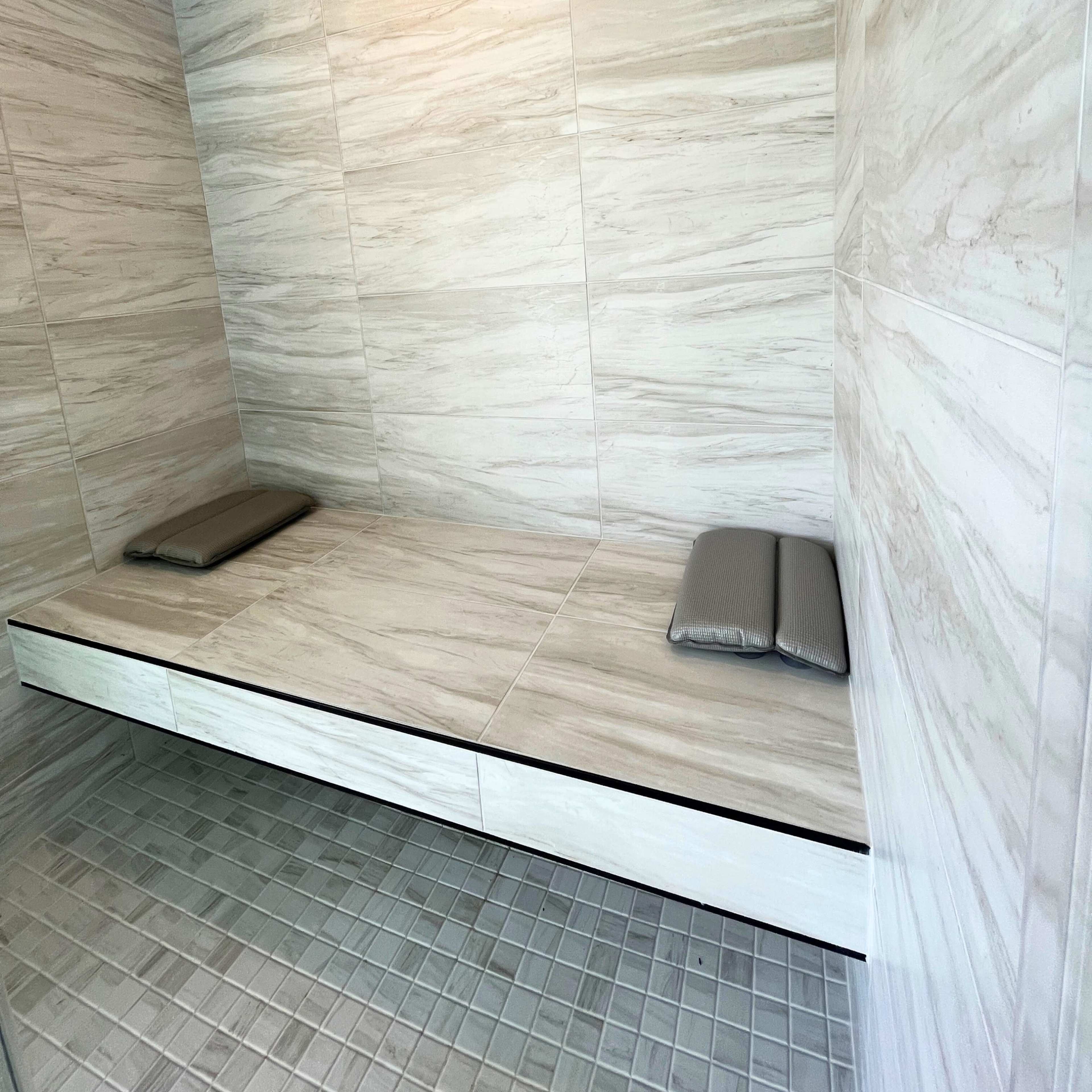 A minimalist sauna room with two padded benches and smooth, light-colored stone walls.
