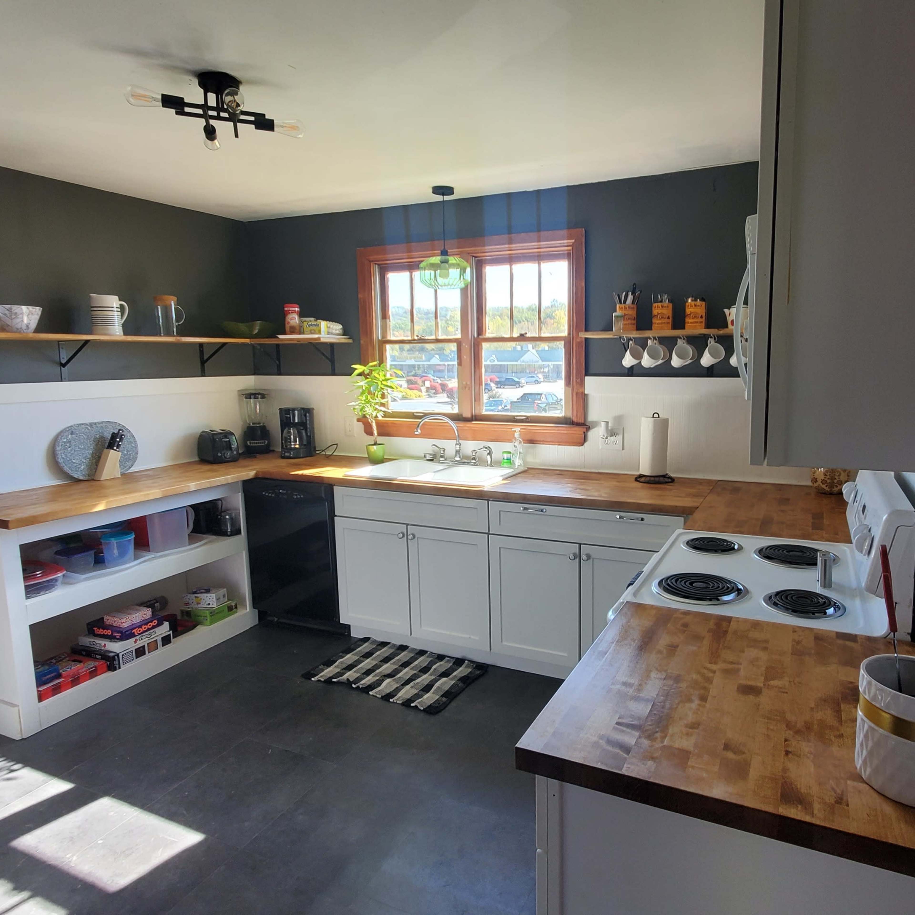 A kitchen with wooden countertops, white cabinetry, and a window above the sink, featuring a simple layout and a few decorative items on shelves.