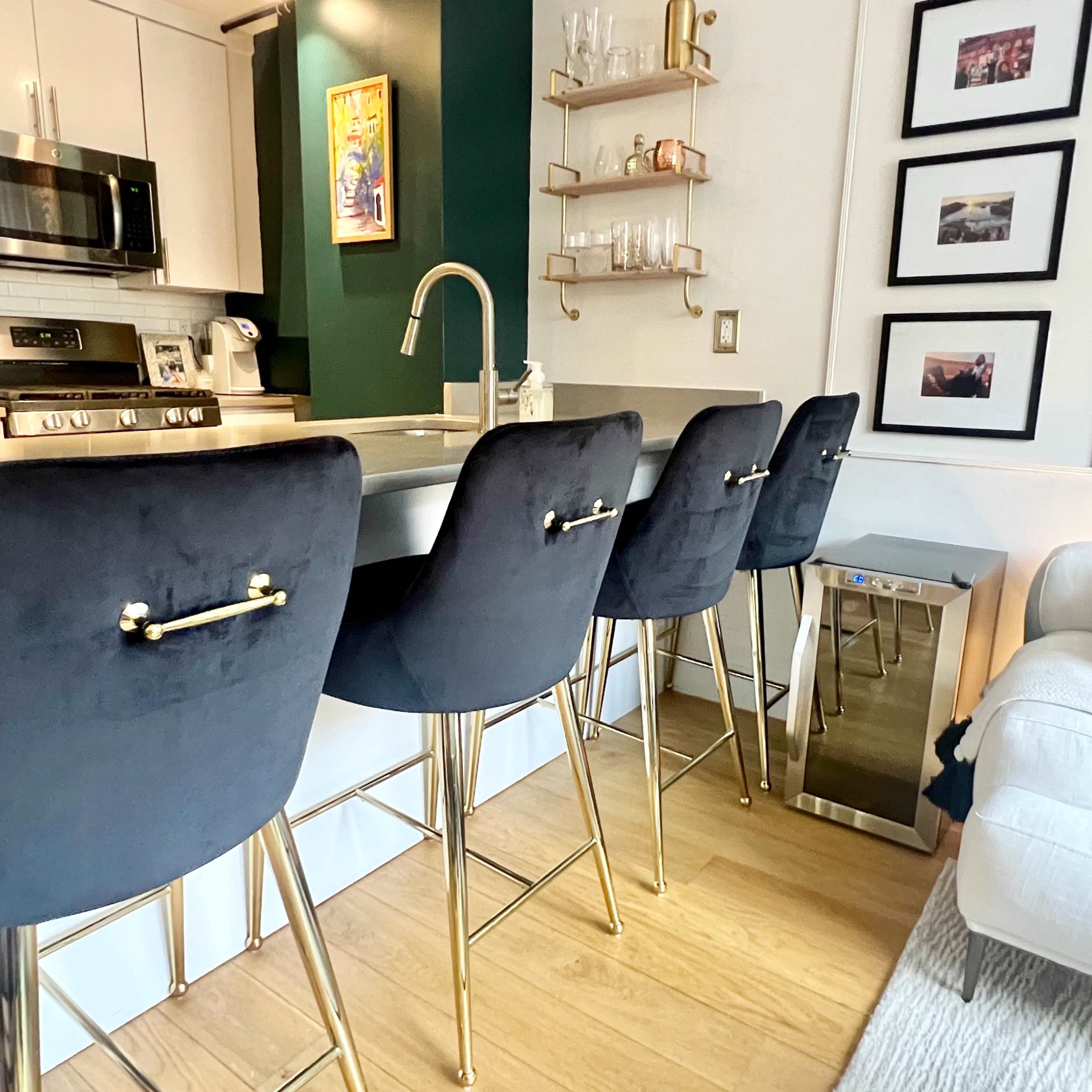 A modern kitchen with a small breakfast bar featuring four black upholstered stools with gold accents and a sleek countertop.