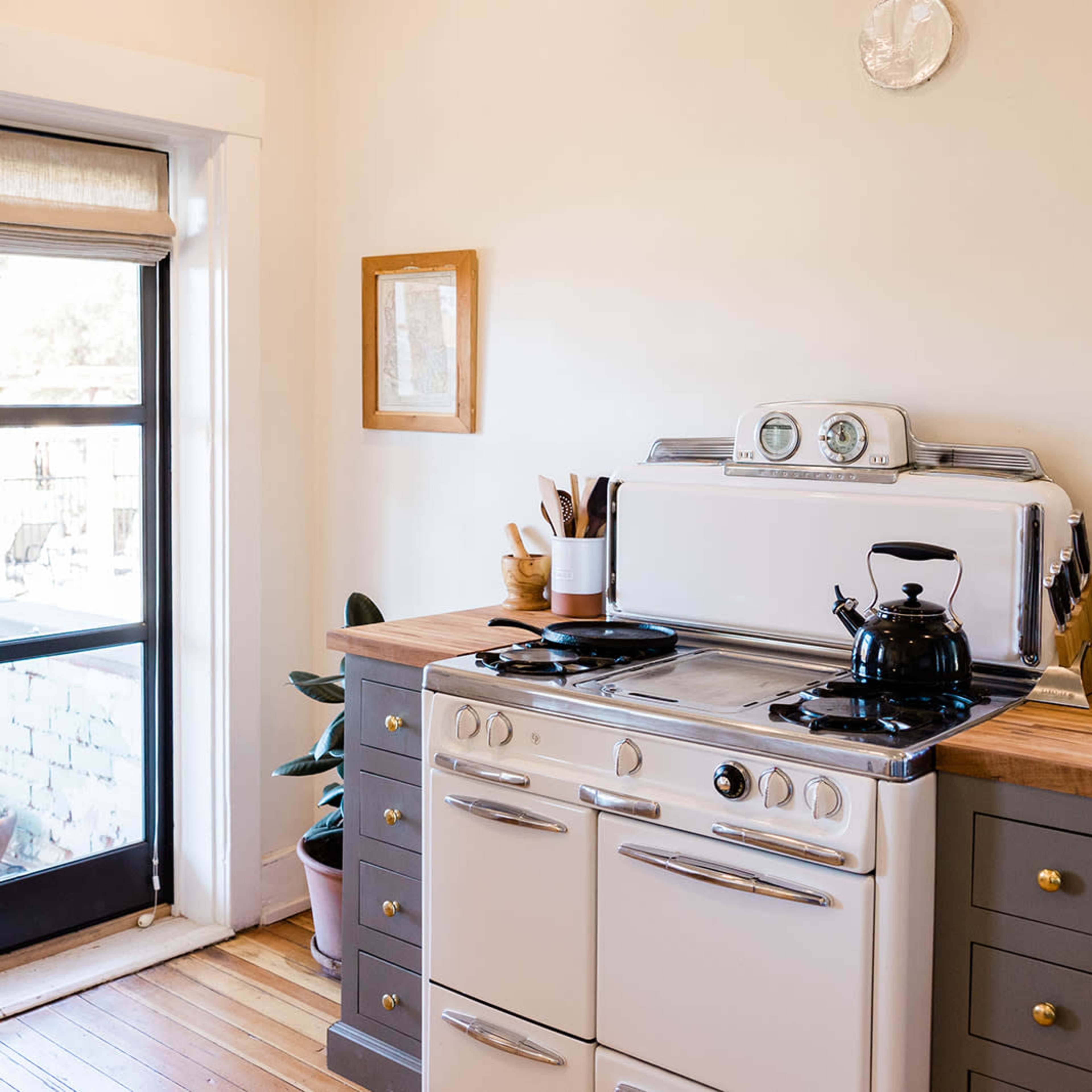 A bright kitchen features a white stove, wooden countertop, and a window with a view of the outdoors.