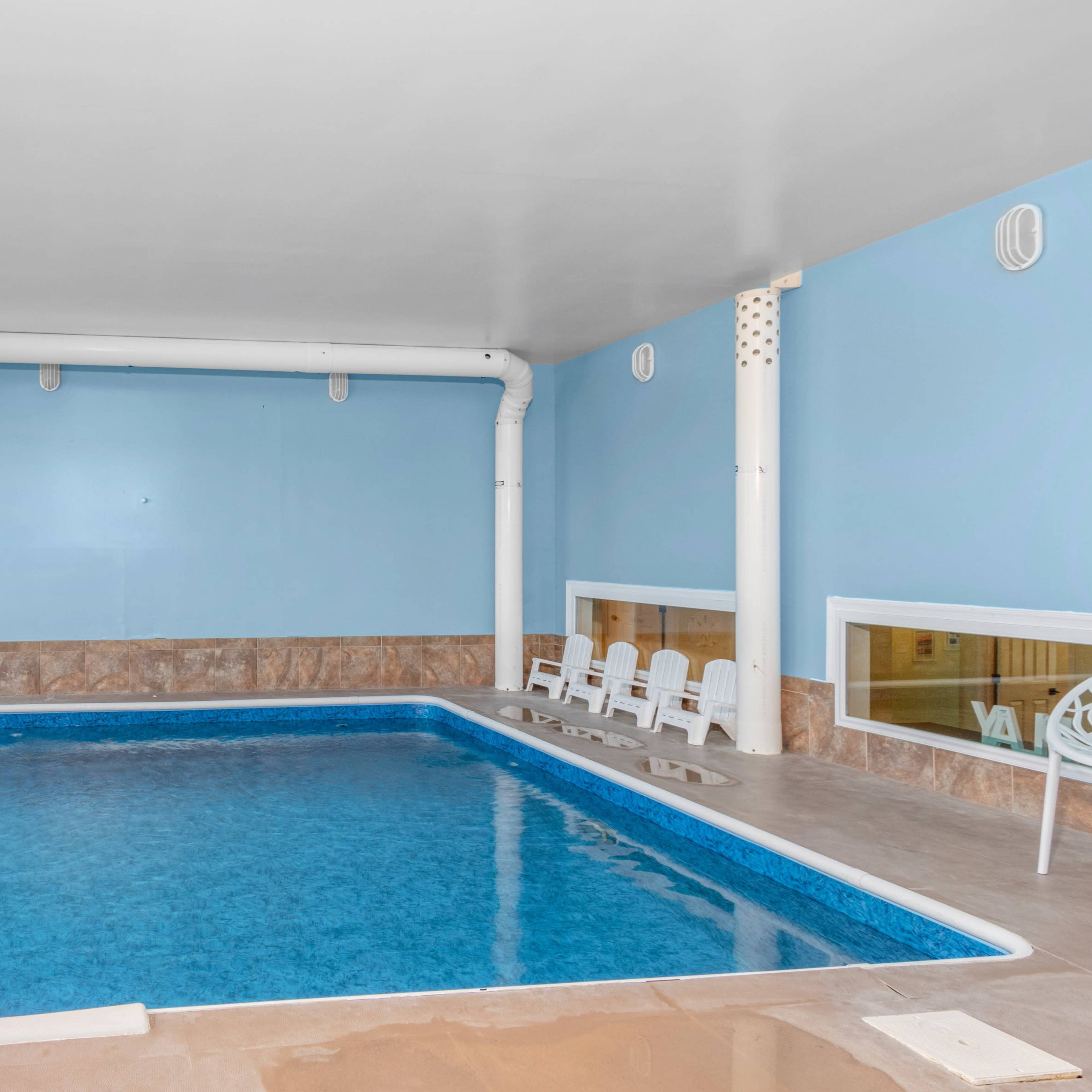 An indoor swimming pool is situated in a room with large windows, allowing natural light to illuminate the blue walls and tan tile flooring.