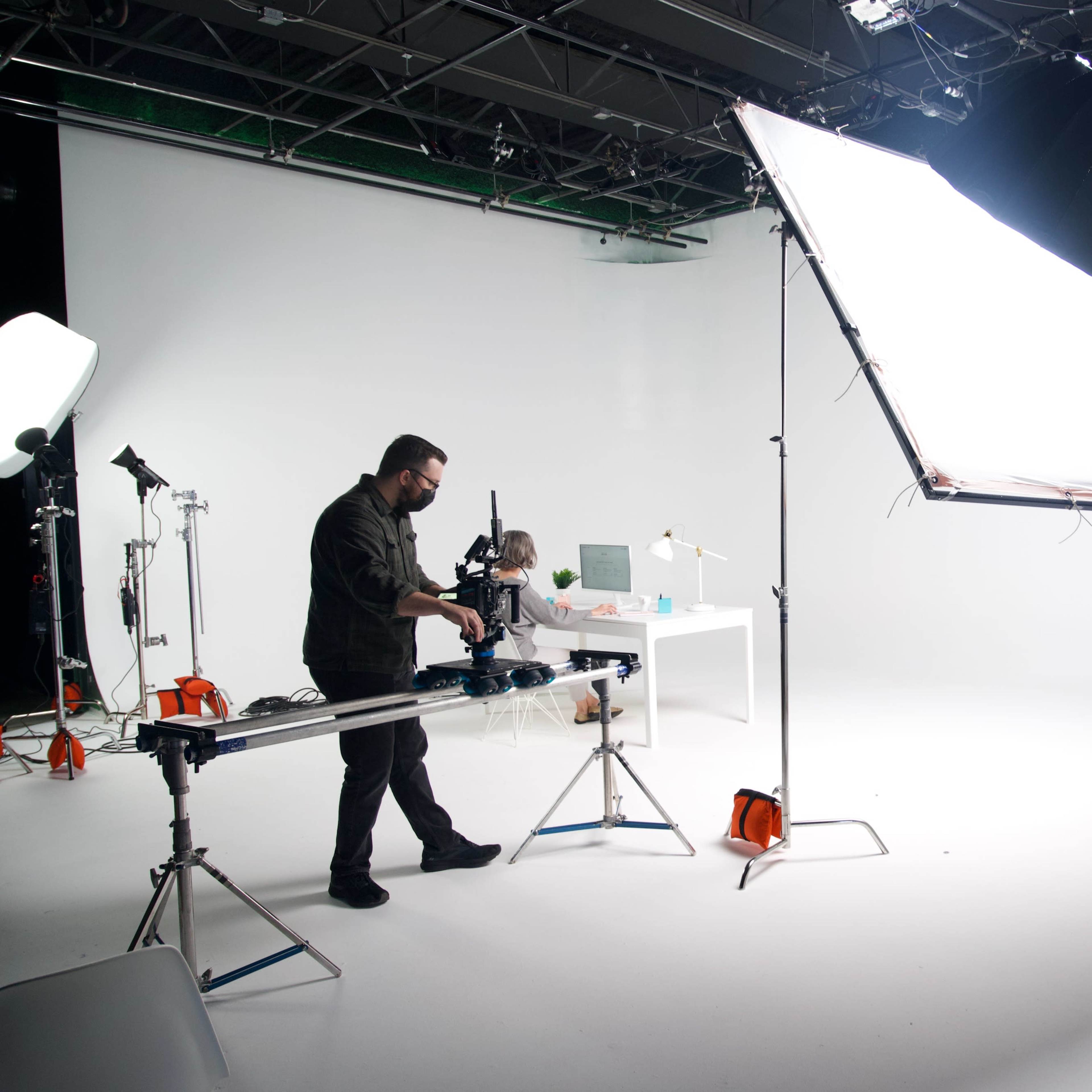 A photographer sets up equipment in a well-lit studio with a large light panel and a backdrop for a photoshoot.